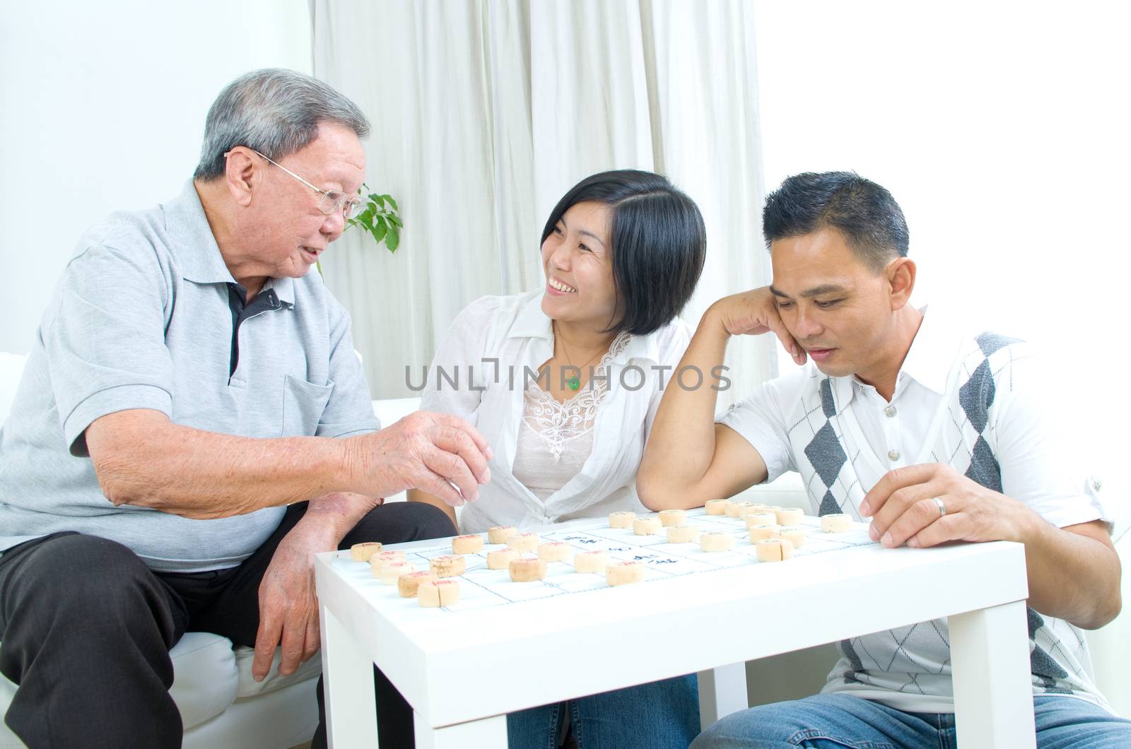 Chinese family playing Chinese chess at home, senior father with his  adult son and daughter.