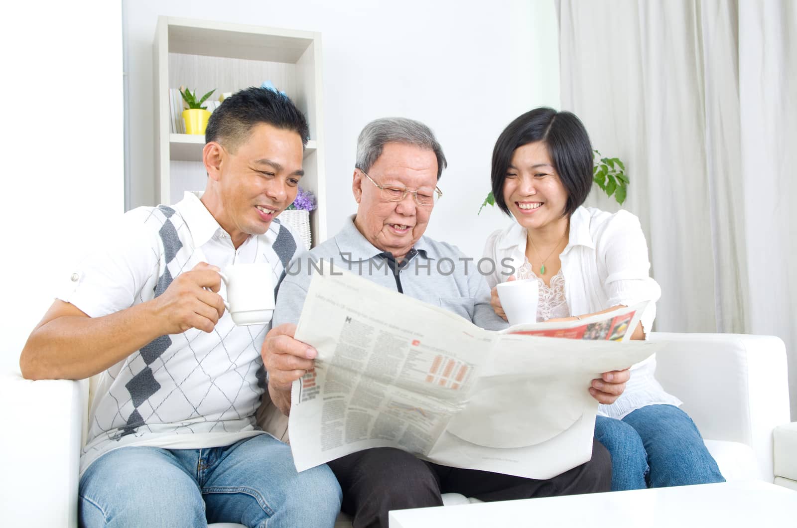 Portrait of chinese family reading newspaper together at home. Mature 80s senior man and his children.