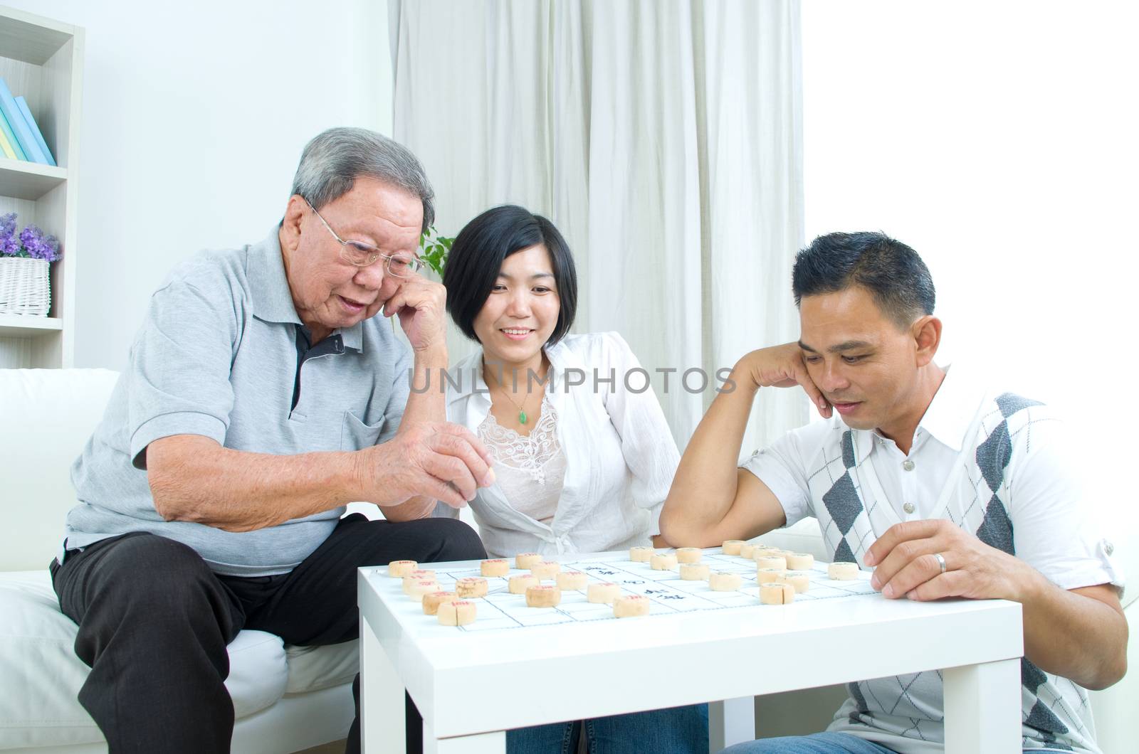 Chinese family playing Chinese chess at home, senior father with his  adult son and daughter.