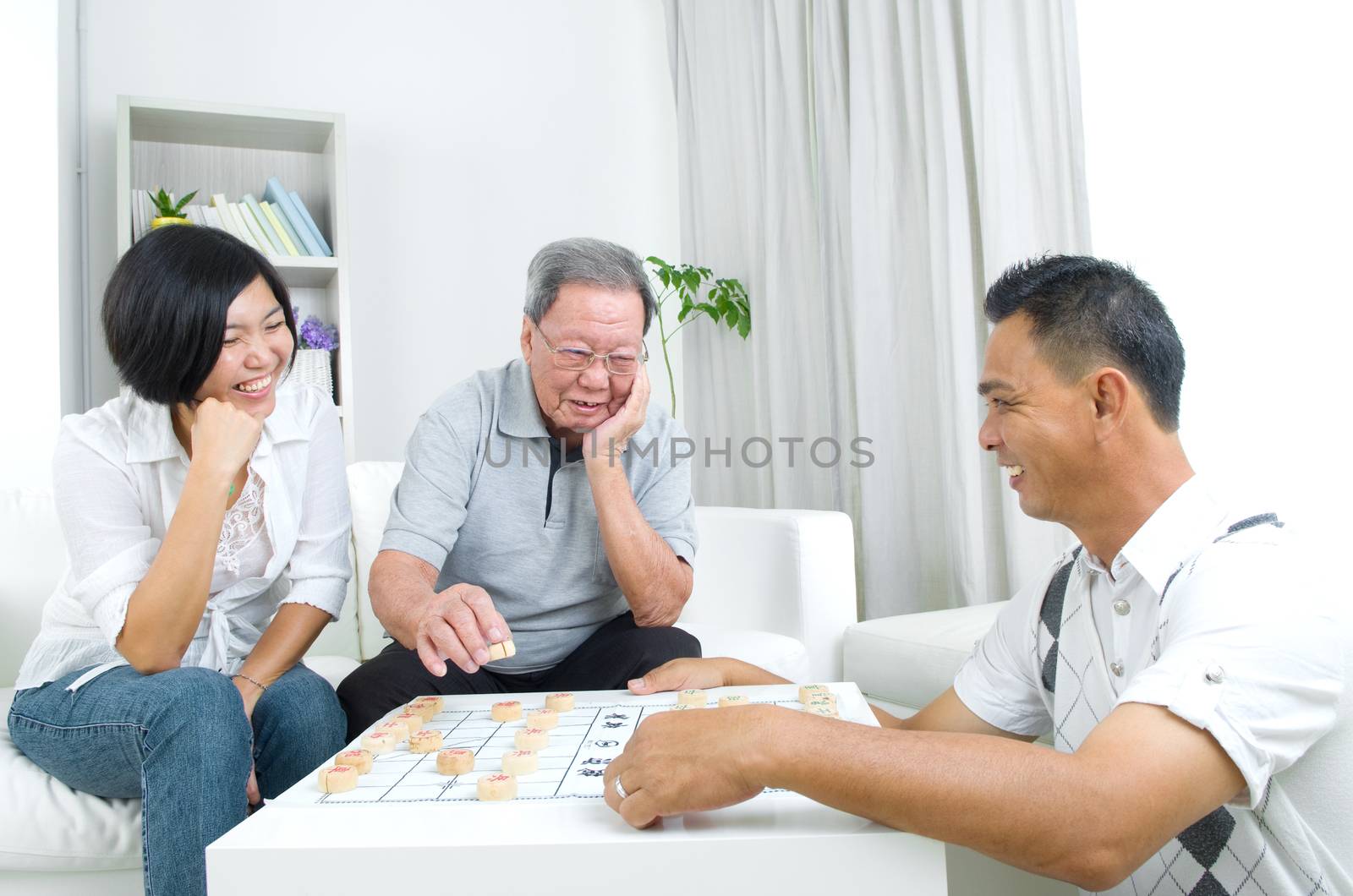 Chinese family playing Chinese chess at home, senior father with his  adult son and daughter.