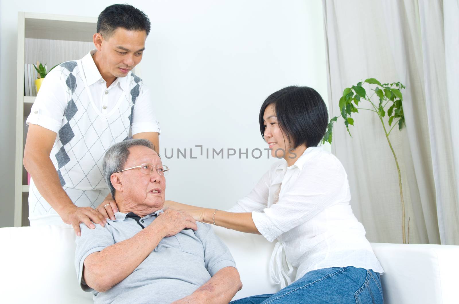 Asian old man shoulder pain, sitting on sofa , daughter and son massaging their father shoulder. Chinese family, senior retiree indoors living lifestyle at home.