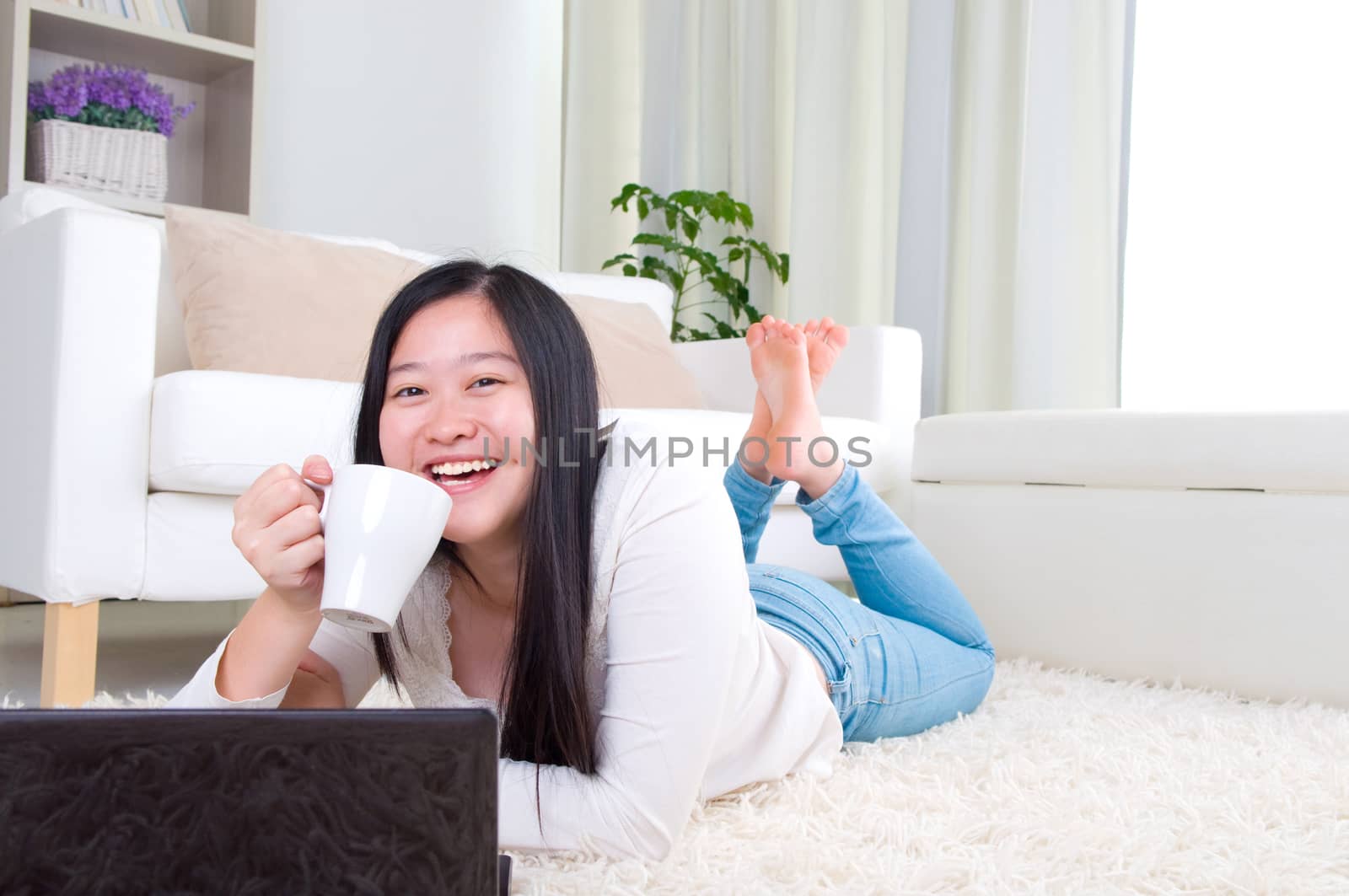 Portrait of attractive Asian girl using laptop and drinking coffe. Young woman indoors living lifestyle at home.