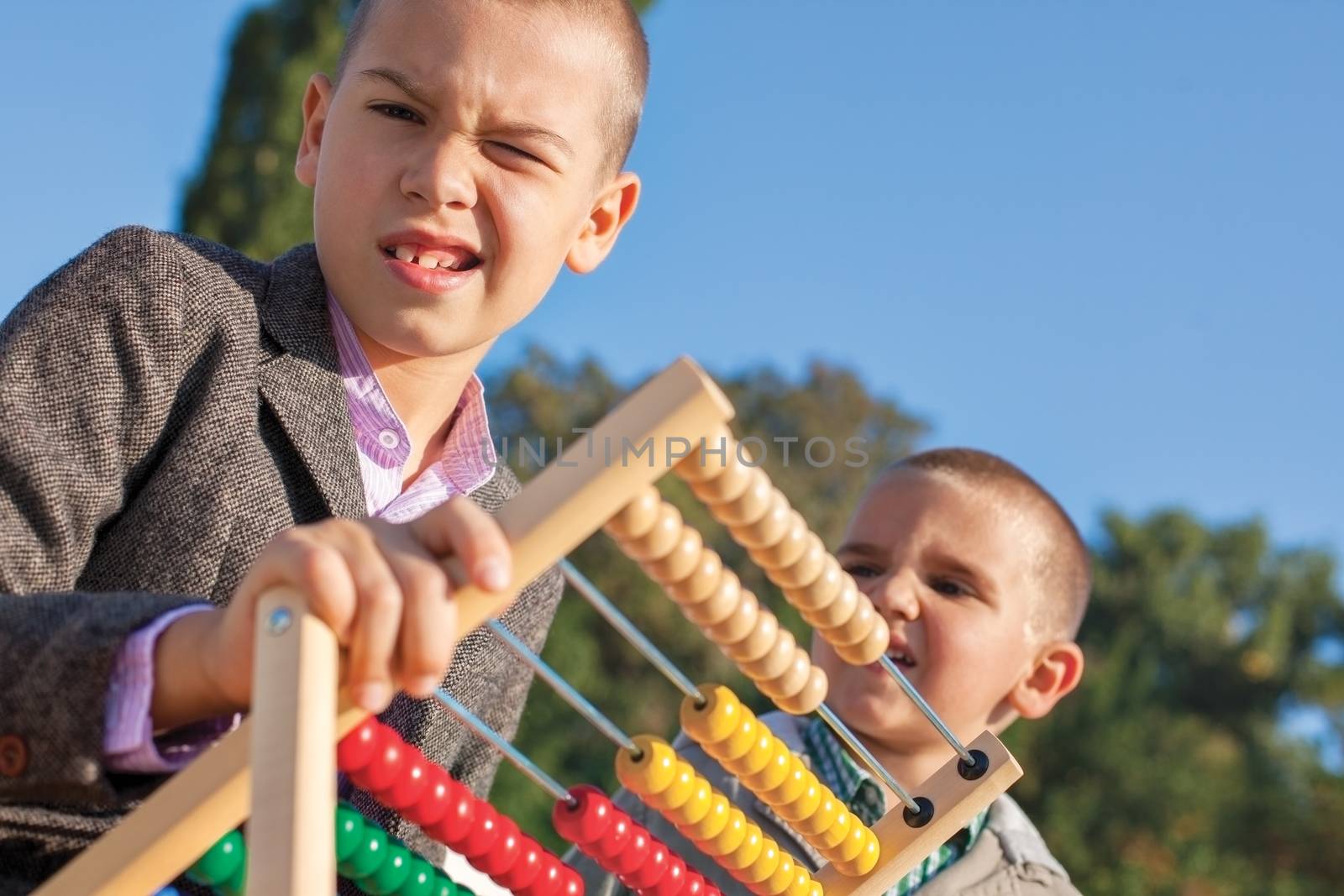 Back to school two confused little boys playing with wooden abacus in the park. One arround seven, the ather four.