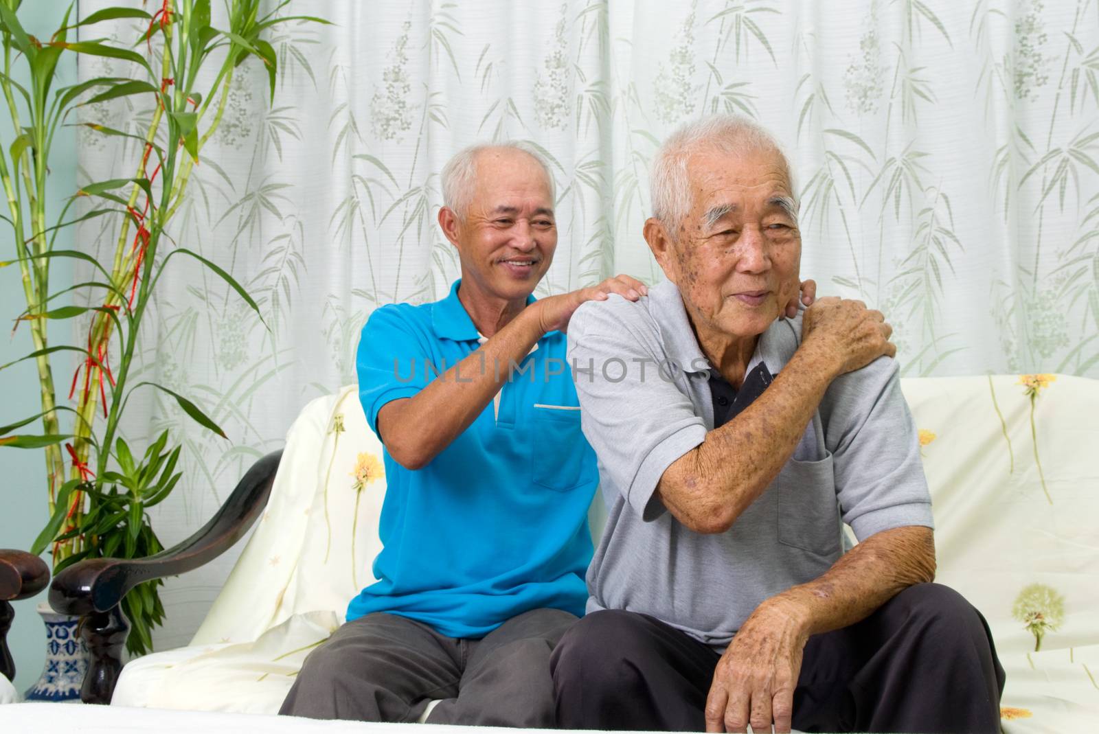 Asian old man shoulder pain, sitting on sofa , son massaging father shoulder. Chinese family, senior retiree indoors living lifestyle at home.