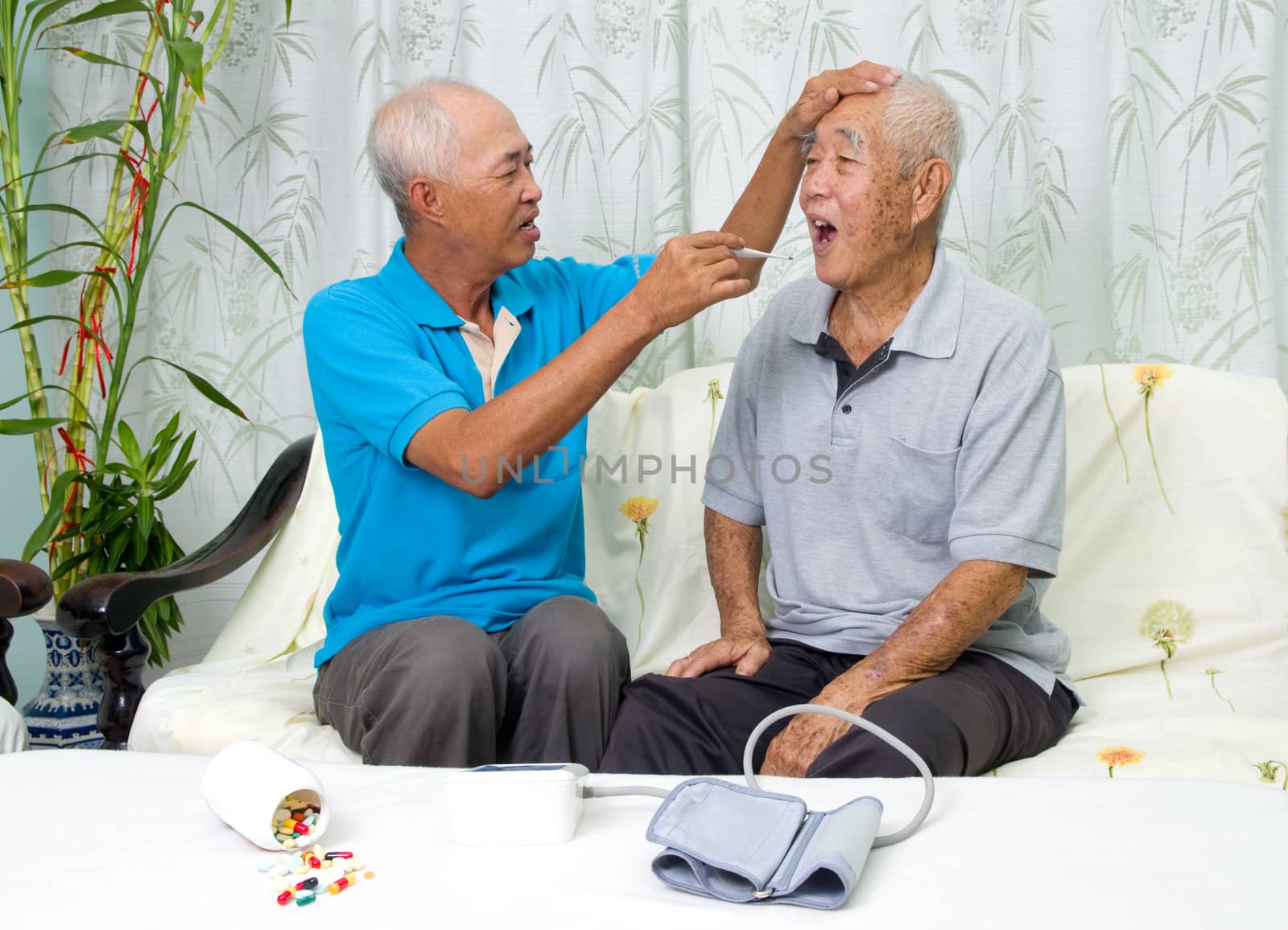 Asian man is checking his father's body temperature with a digital thermometer.