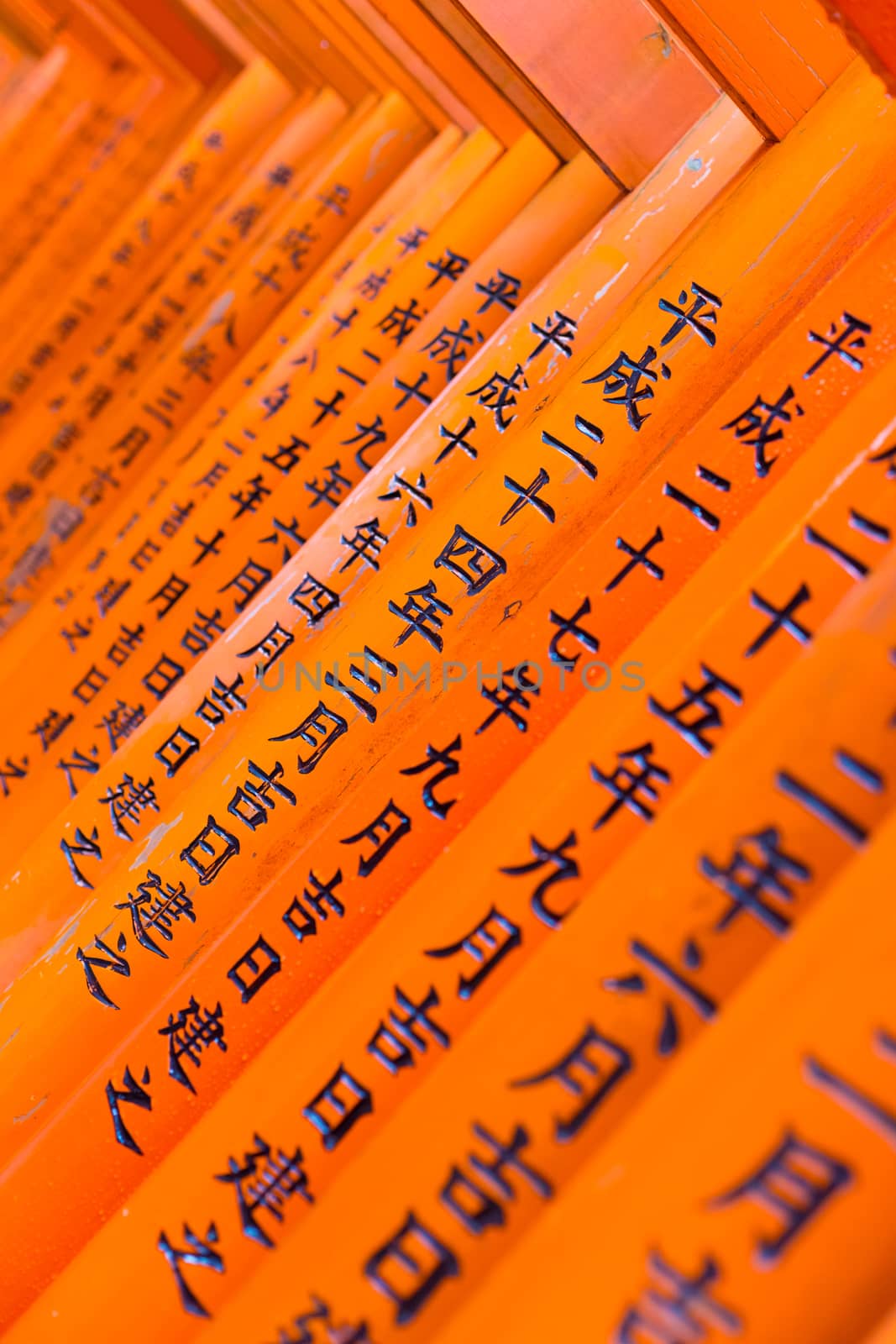 Red wooden Tori Gate at Fushimi Inari Shrine in Kyoto, Japan. Selective focus on traditional japanese writing.