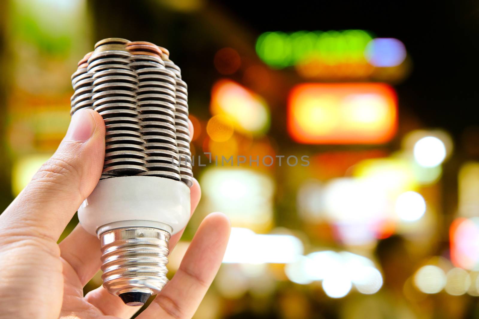 hand holding coin light bulb and night lights on a city street background, energy concept