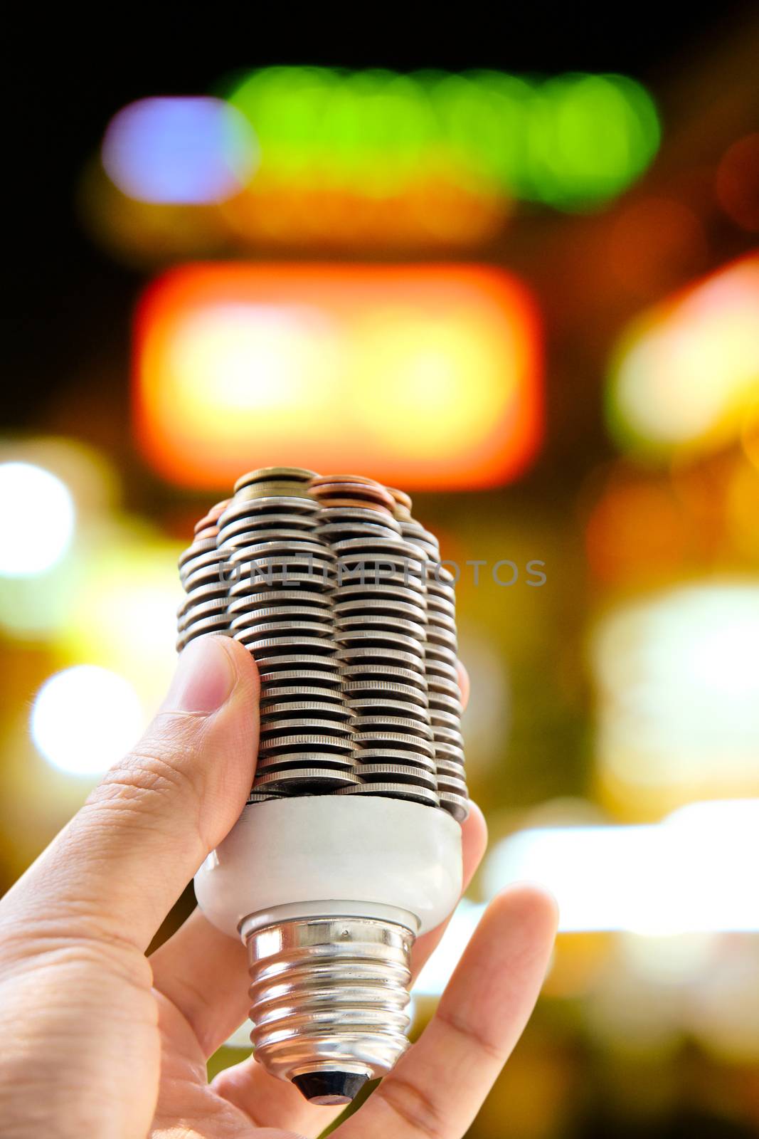 hand holding coin light bulb with defocused city night light background, energy concept