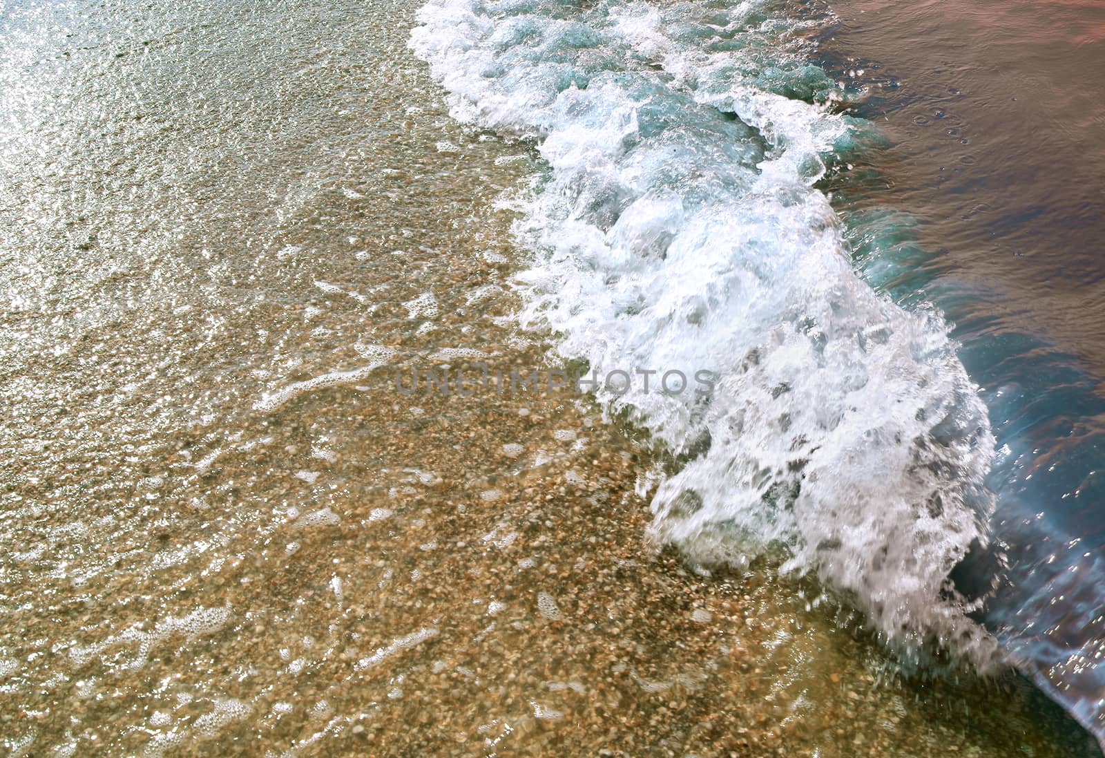 Sea wave rolling on the gravel beach in setting sun