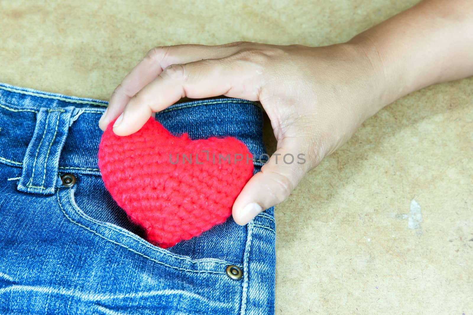 Women took the crochet heart red color out of a blue jeans pocket.