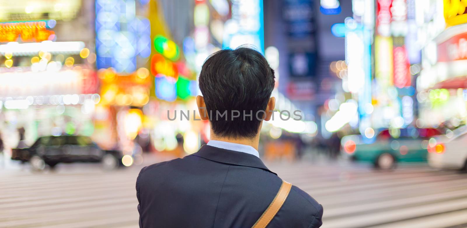 Solitary japanese corporative businessman in suit, after work, waiting on crossroad in Kabukicho, entertainment and red-light district in Shinjuku, Tokyo, Japan. 