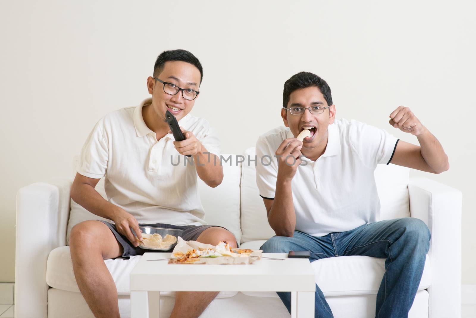 Friendship, technology and home concept. Smiling male friends with remote control and junk food at home.