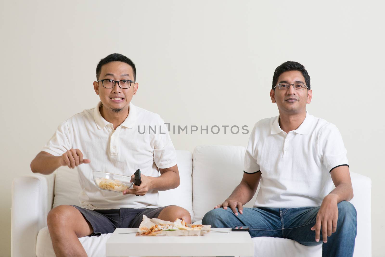 Group of friends sitting on sofa watching TV together at home.