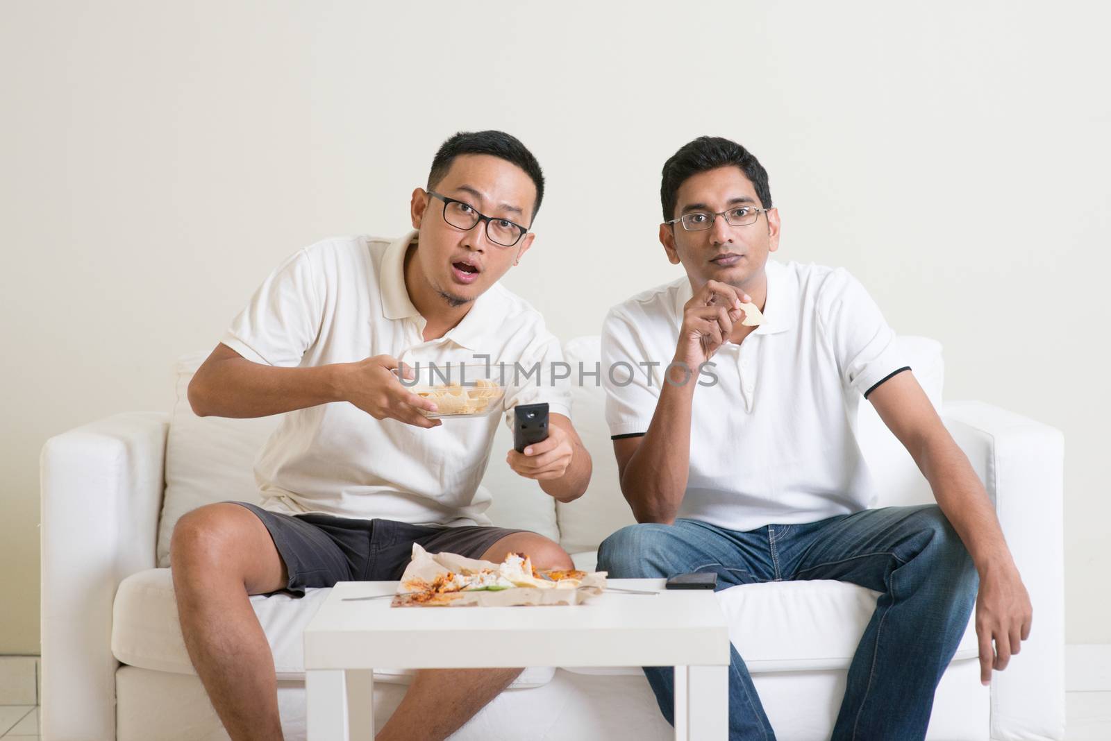 Group of friends sitting on sofa watching football match together at home.