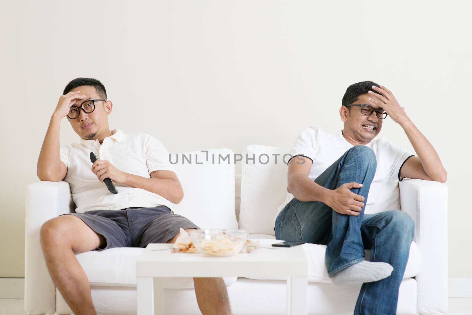 Men sitting on couch watching football match on television together at home.