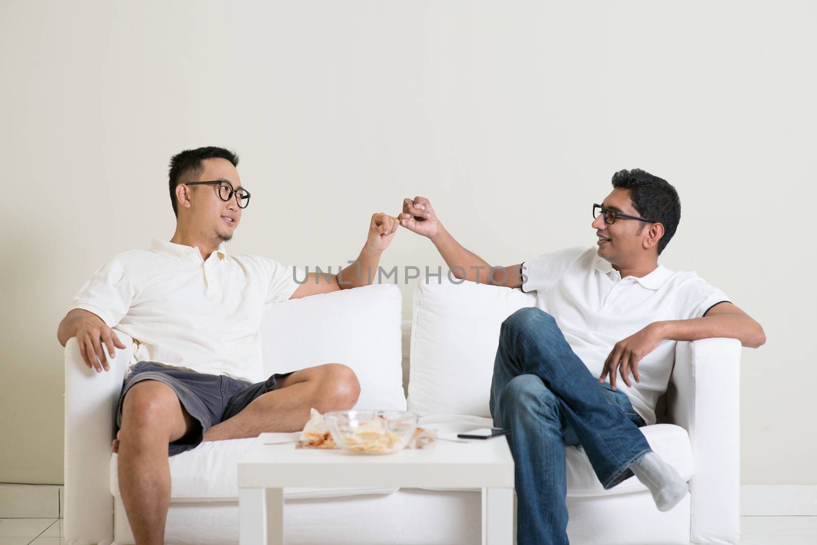 Friends sitting on sofa and giving hand promise at home. Multiracial people friendship.