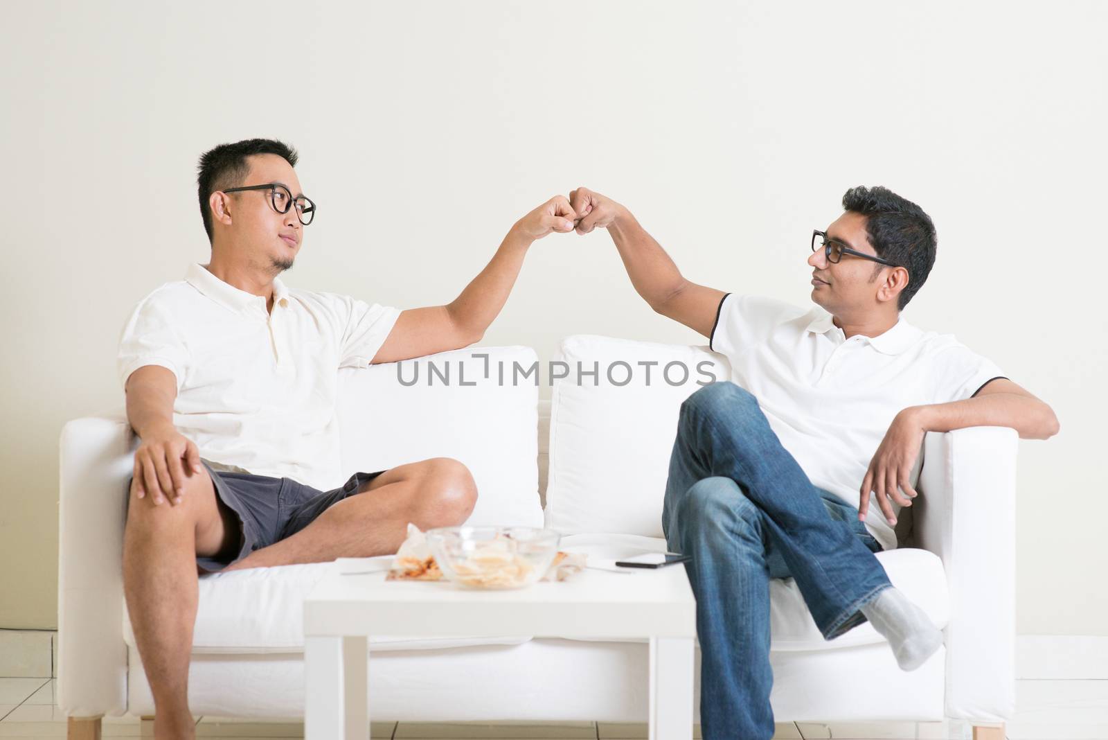 Man sitting on sofa and giving fist bump to friend at home. Multiracial people friendship.