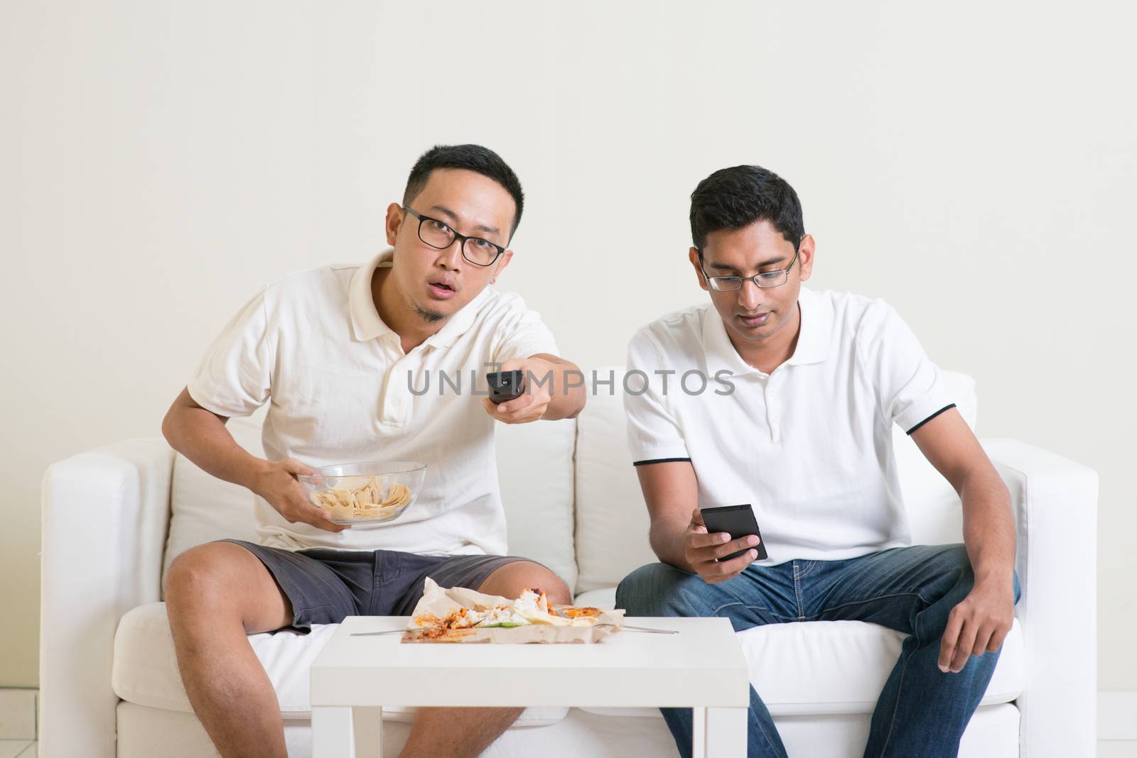 Friendship, technology and home concept. Two male friends with remote control and junk food at home.
