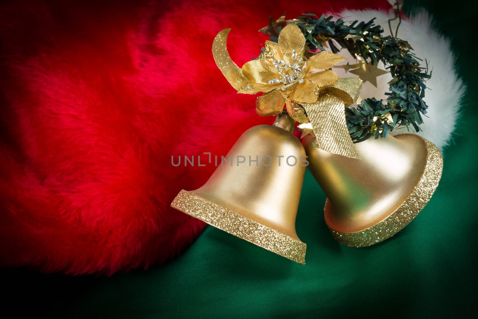 Santa Claus hat and gold bells on green cloth with dark vignette