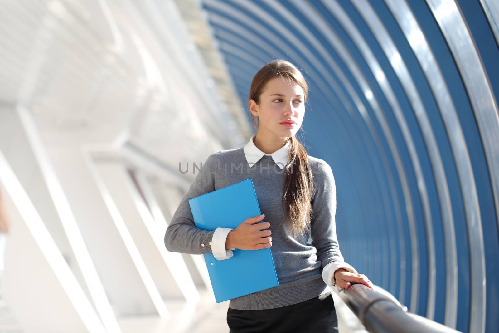 Young Businesswoman with folder standing in corridor of modern office building