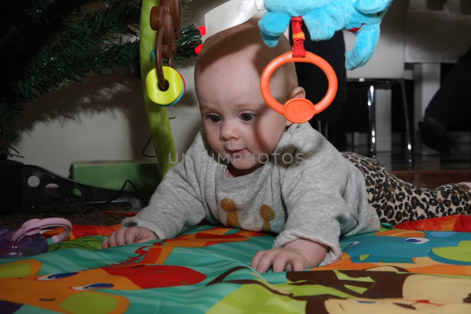 Happy baby girl playing on the floor surrounded surrounded by toys
