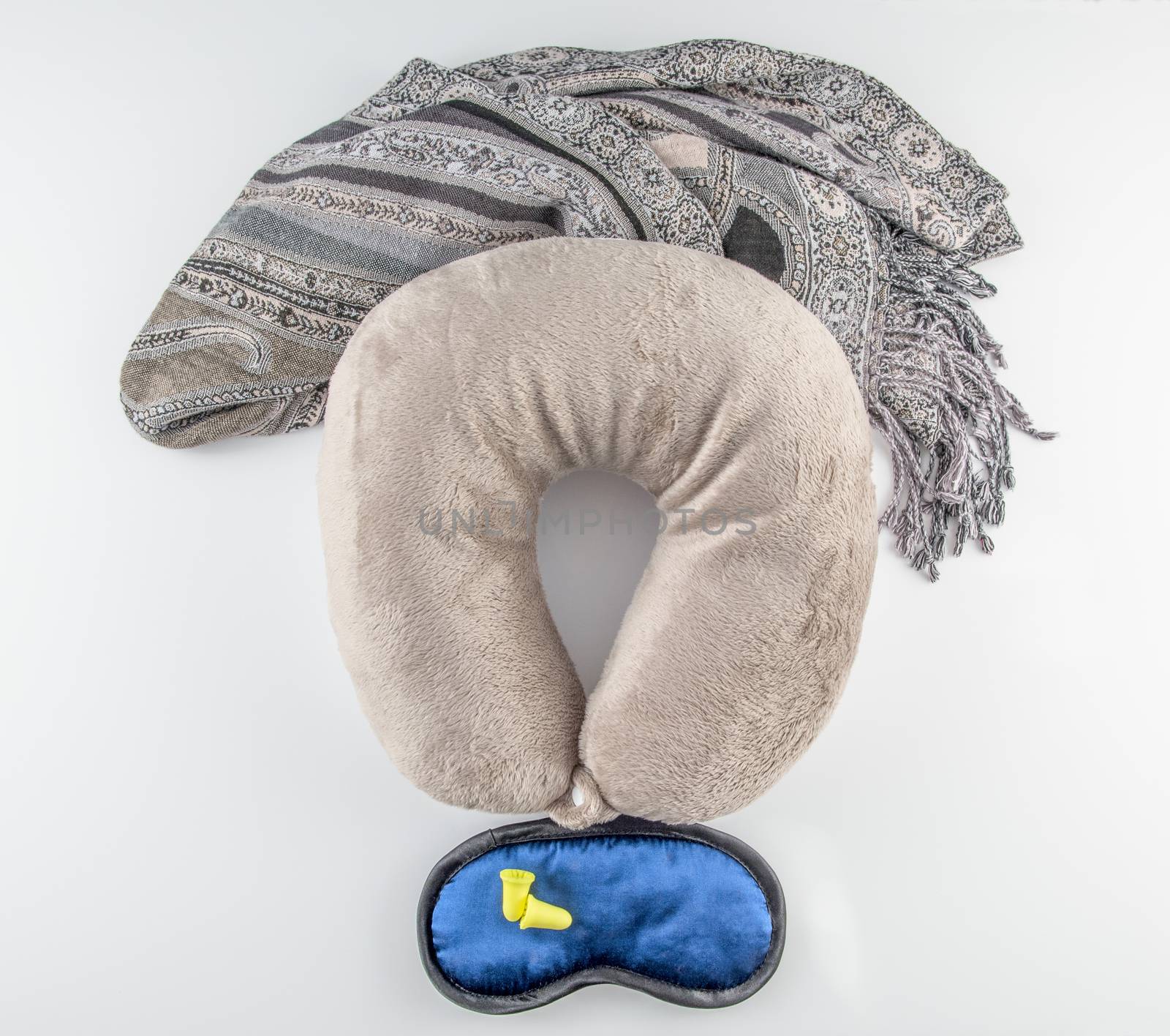 Airplane travel essentials (pillow, scarf/blanket, sleep mask, and ear plugs) on white background