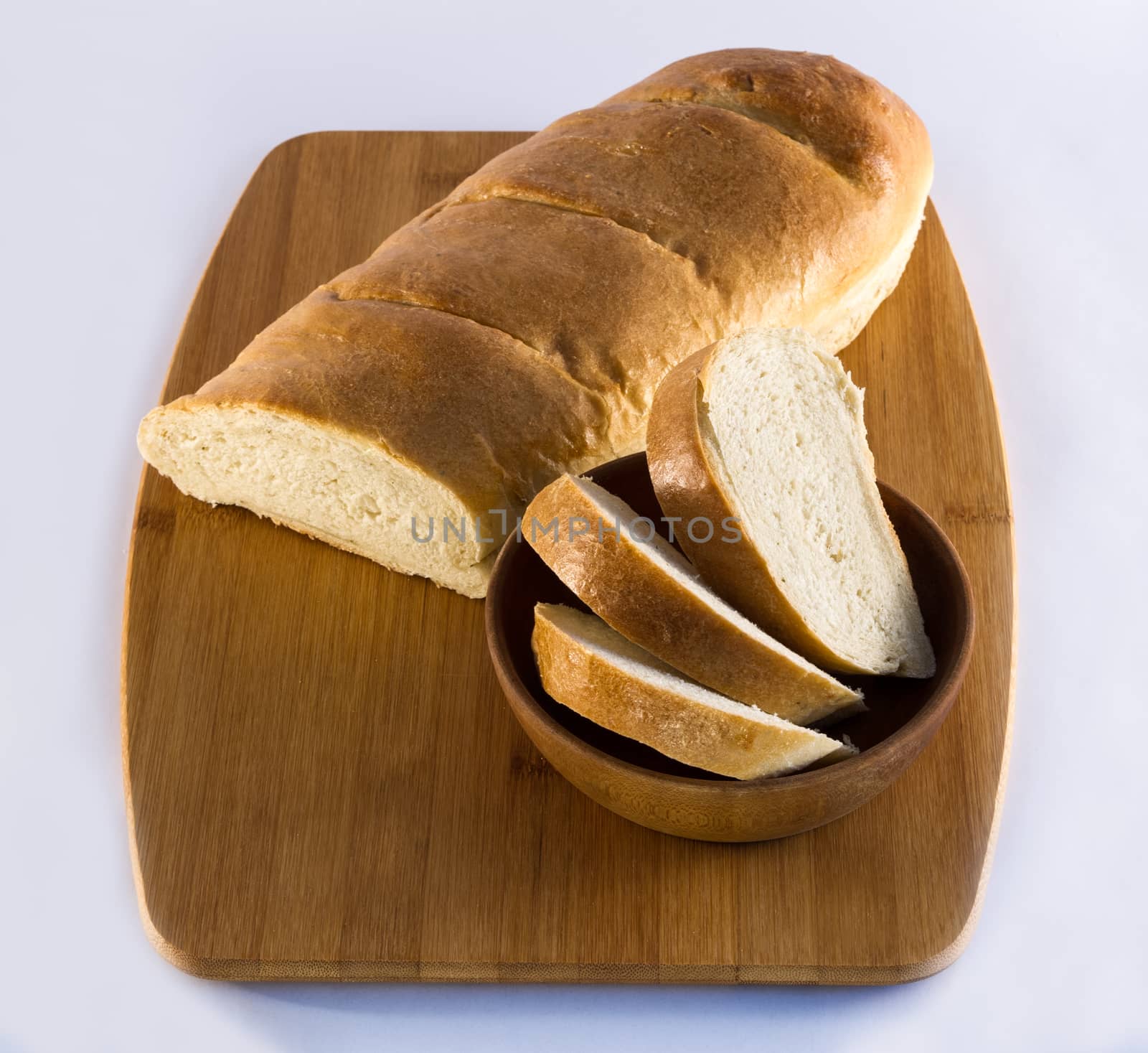 Fresh French bread loaf on wooden cutting board, with sliced bread in wooden bowl