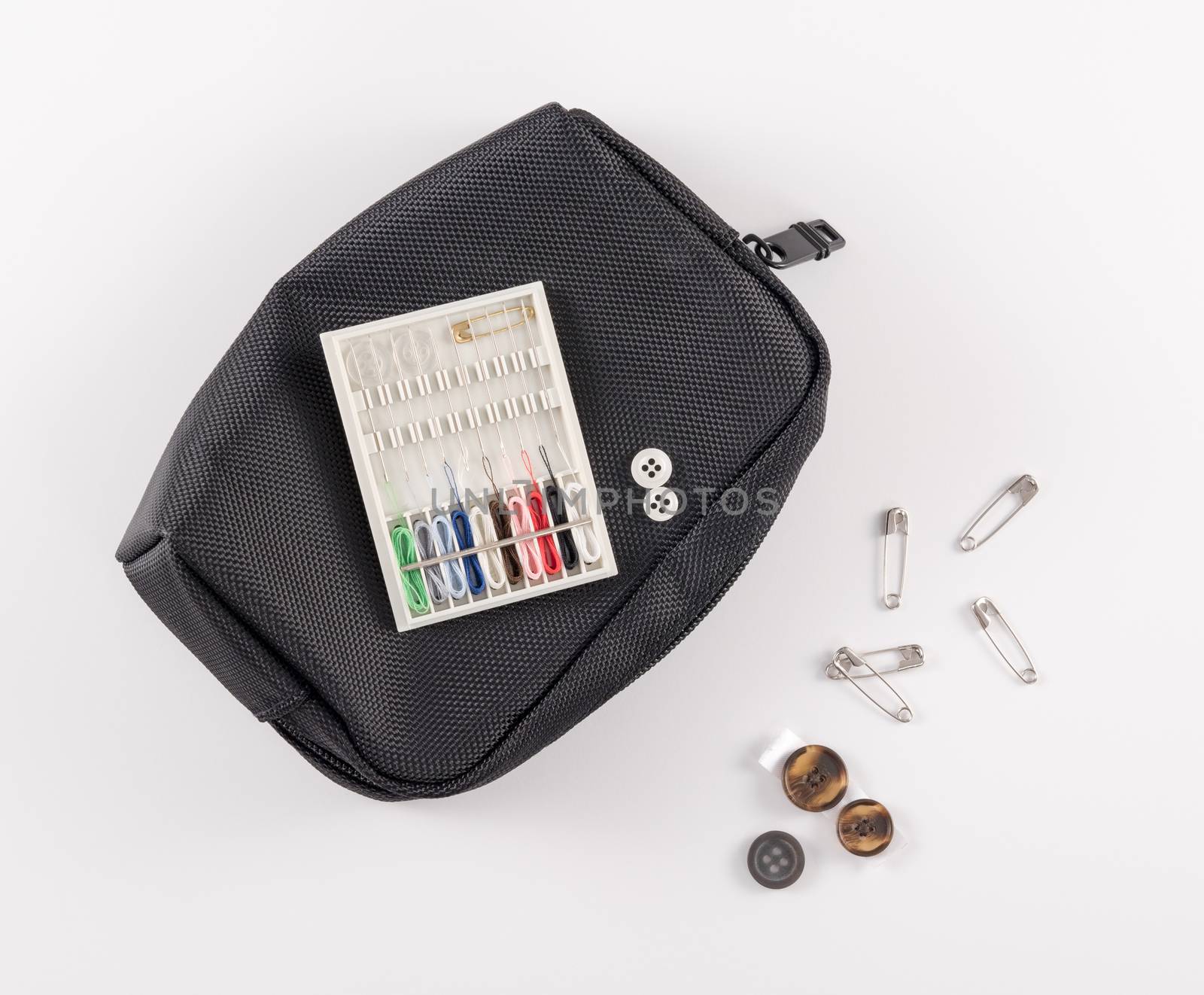 Travel sewing kit with black care, buttons, and safety pins on white background