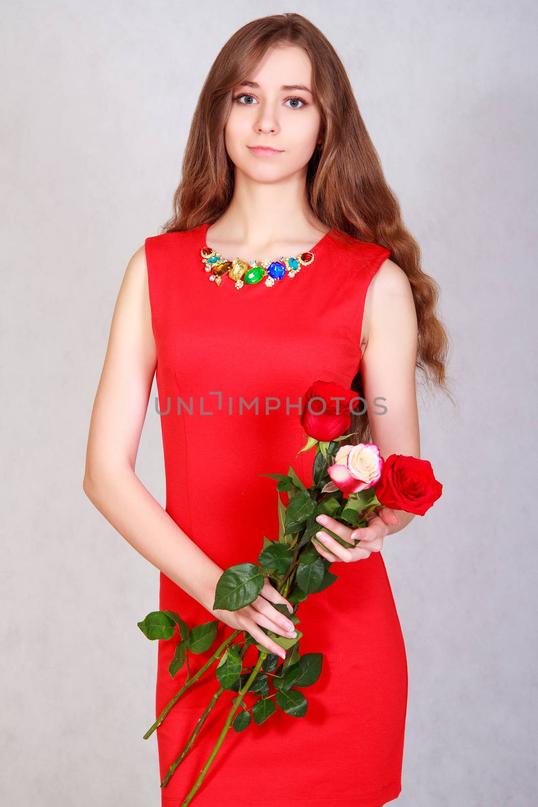 Portrait of a young attractive woman with a bunch of red roses over grey background