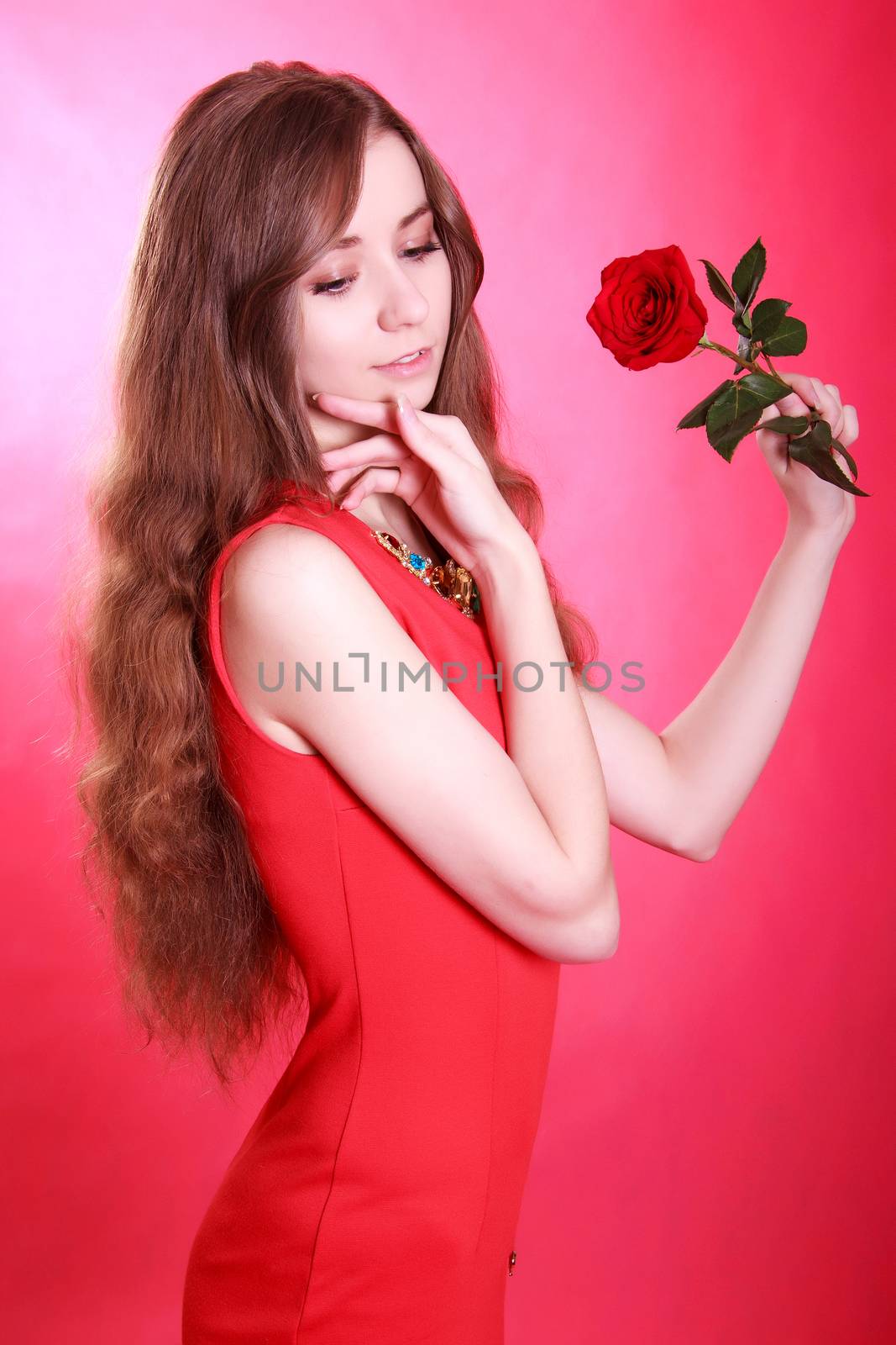 Portrait of a young attractive woman with a red rose over pink background