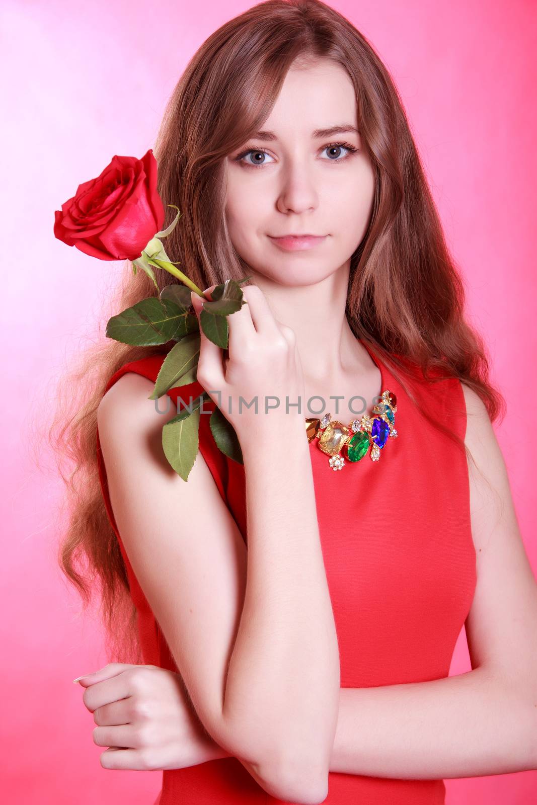 Portrait of a young attractive woman with a red rose over pink background