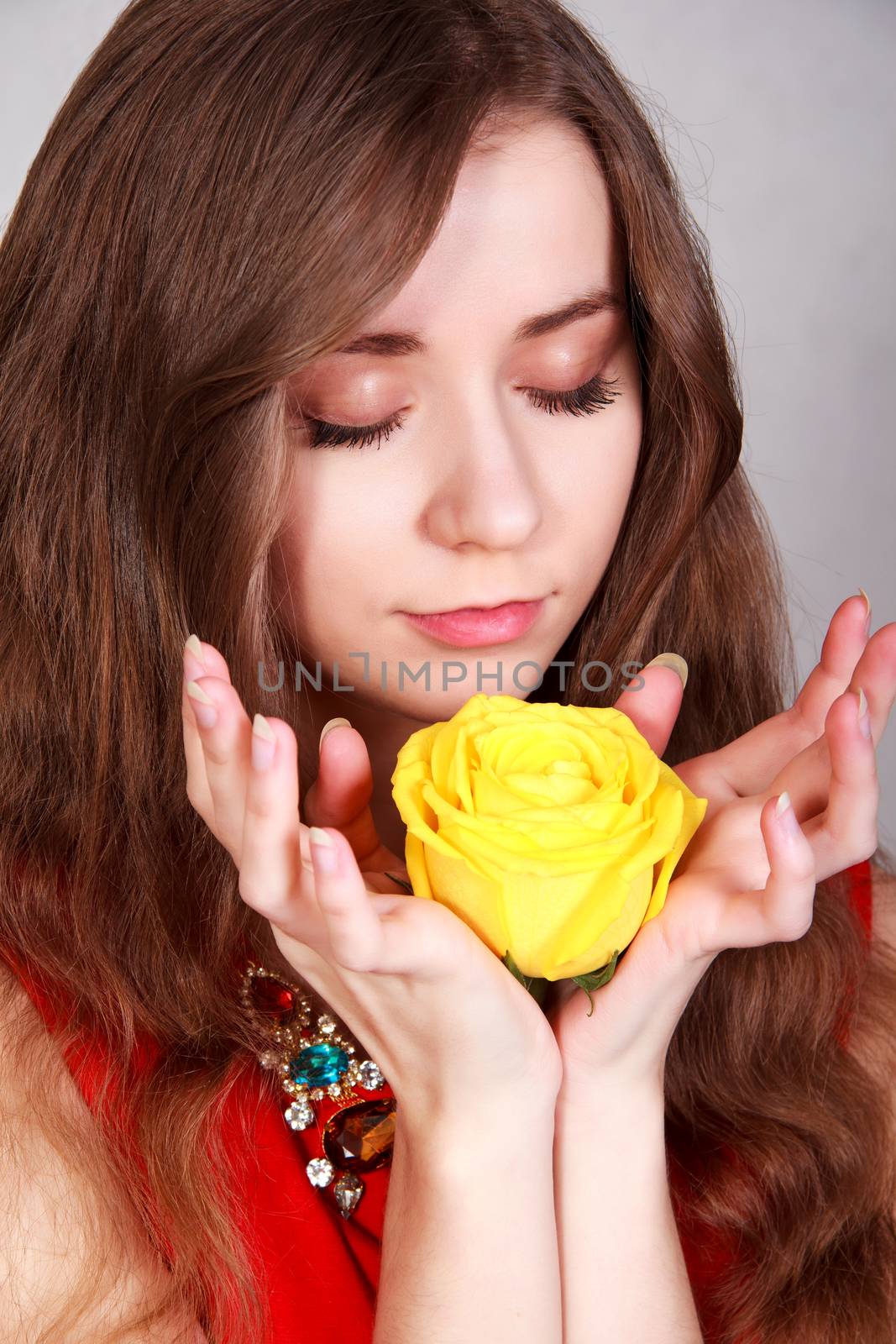 Portrait of a beautiful young woman with a yellow rose over grey background