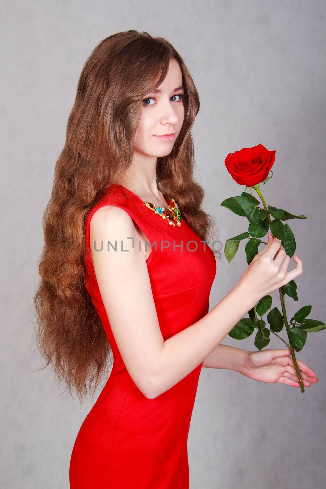 Beautiful young woman with a red rose over grey background