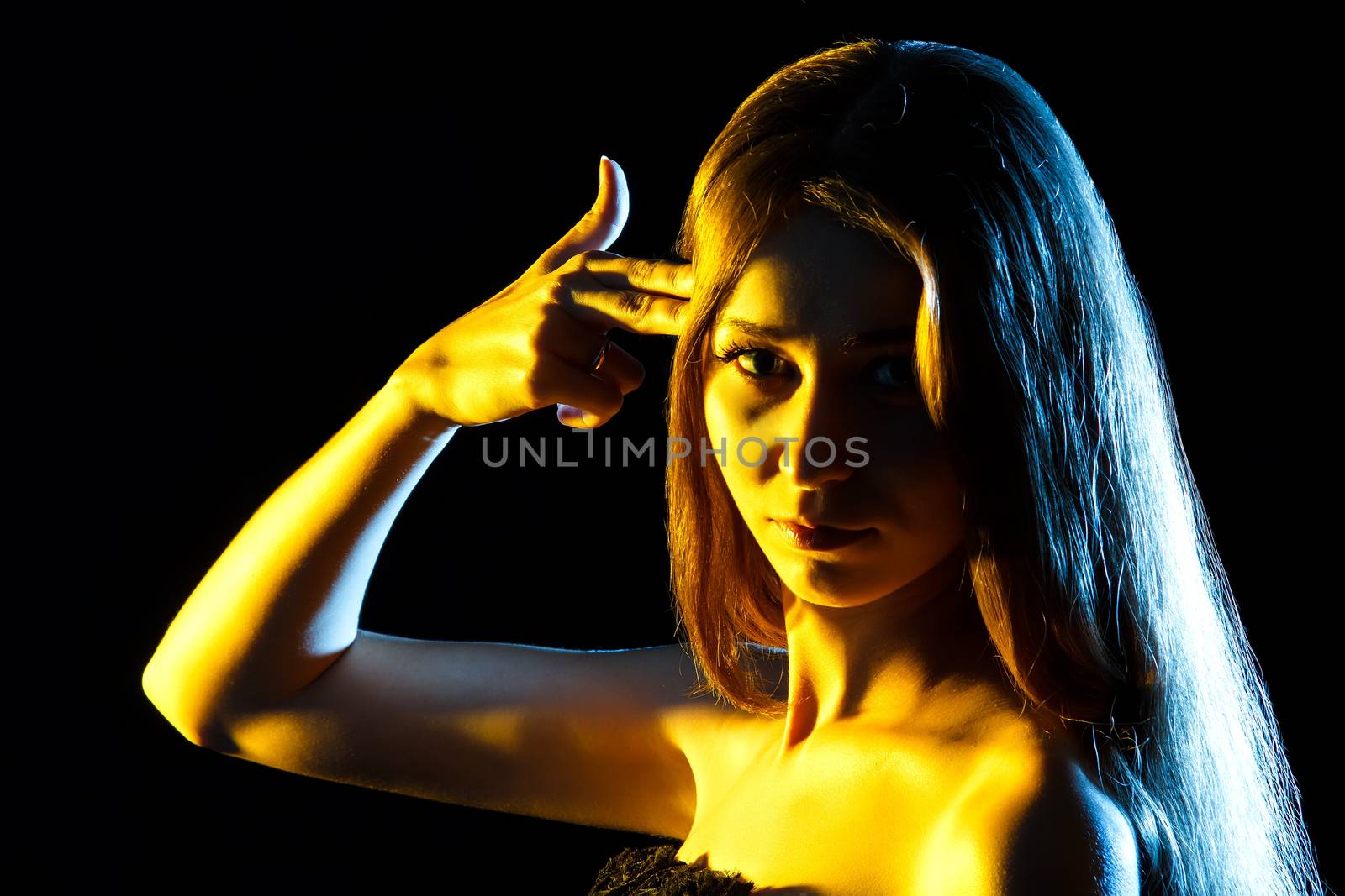 Beautiful young woman in yellow lights pointing fingers to the head like shooting a gun over black background
