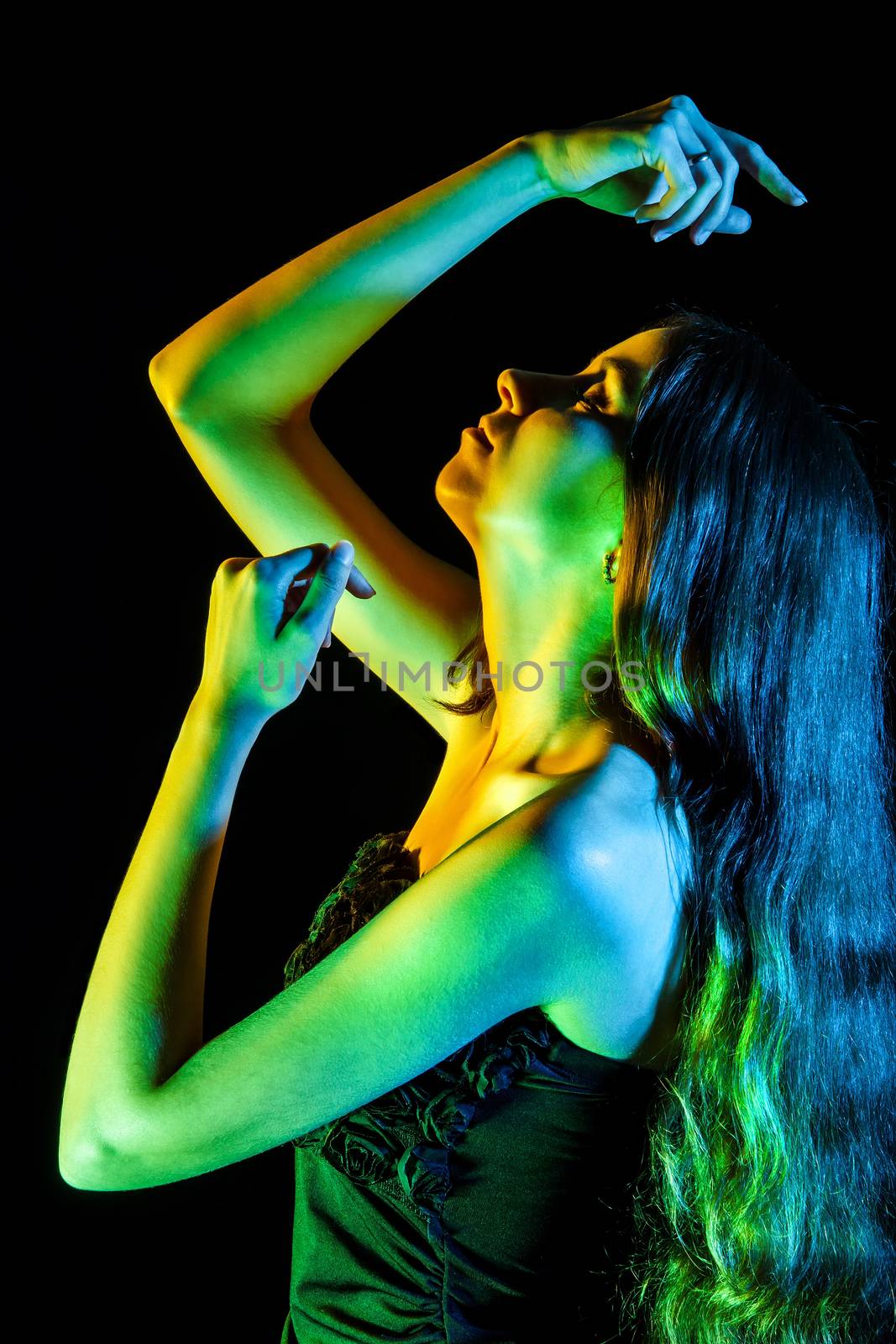 Beautiful young woman in green, blue and yellow lights over black background