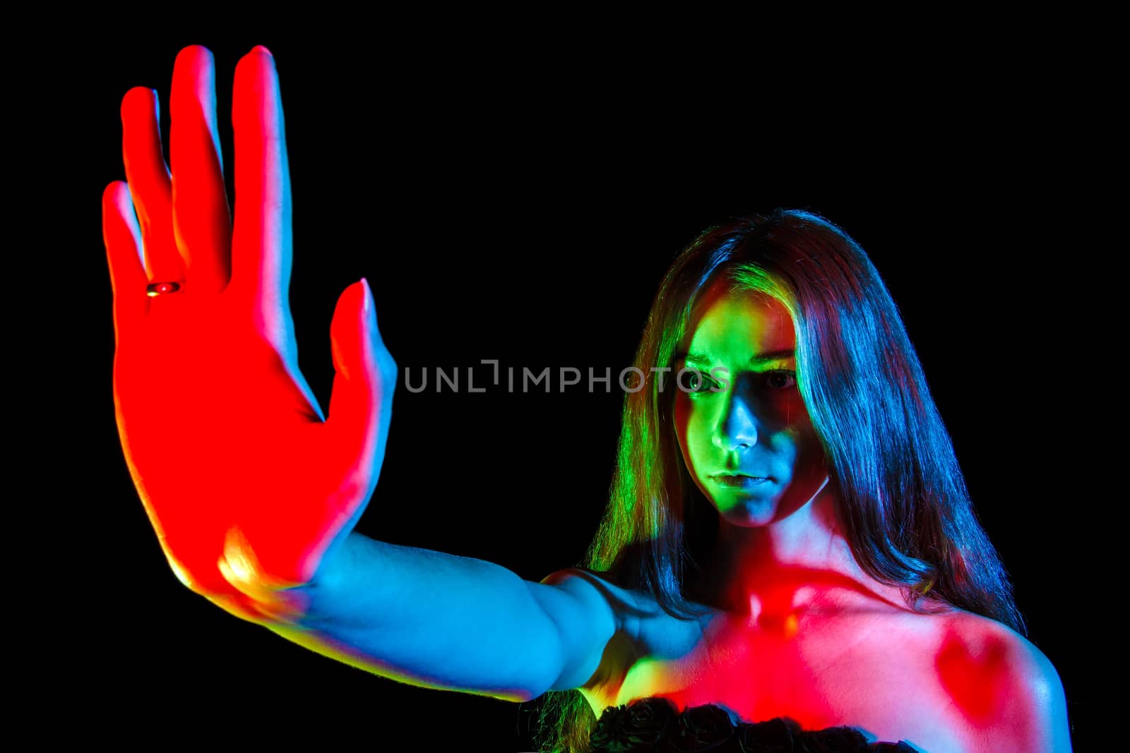 Beautiful young woman in red, green and blue lights showing the stop sign over black background