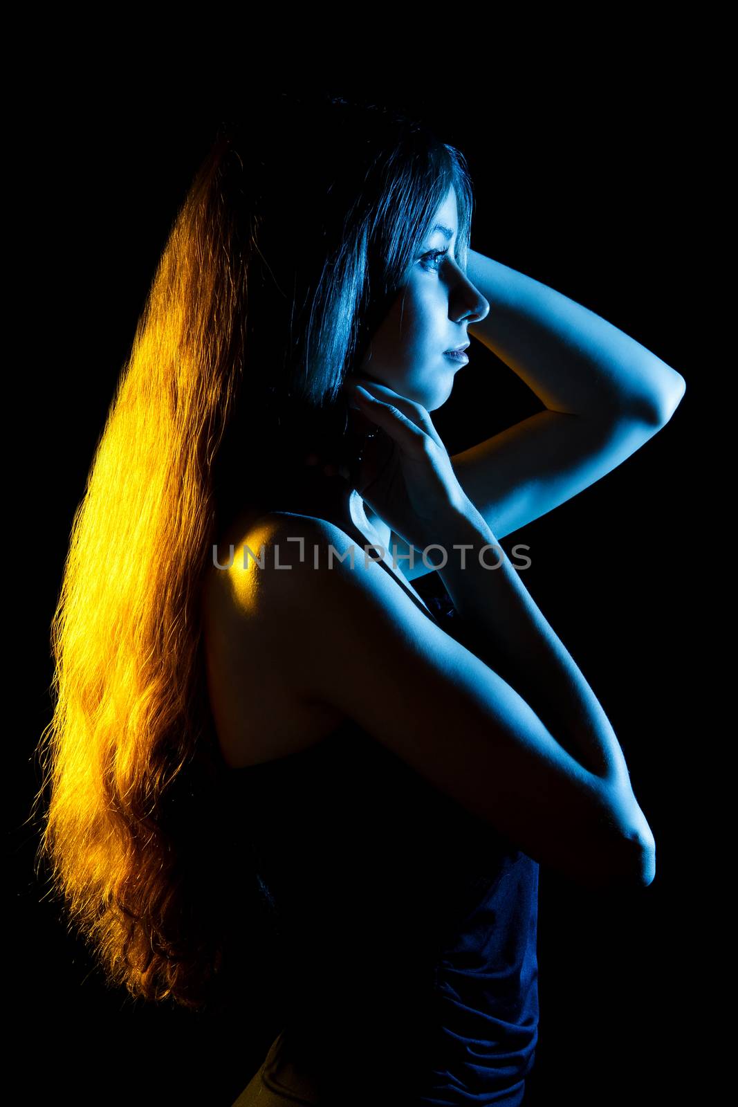 Beautiful young woman in blue and yellow lights over black background