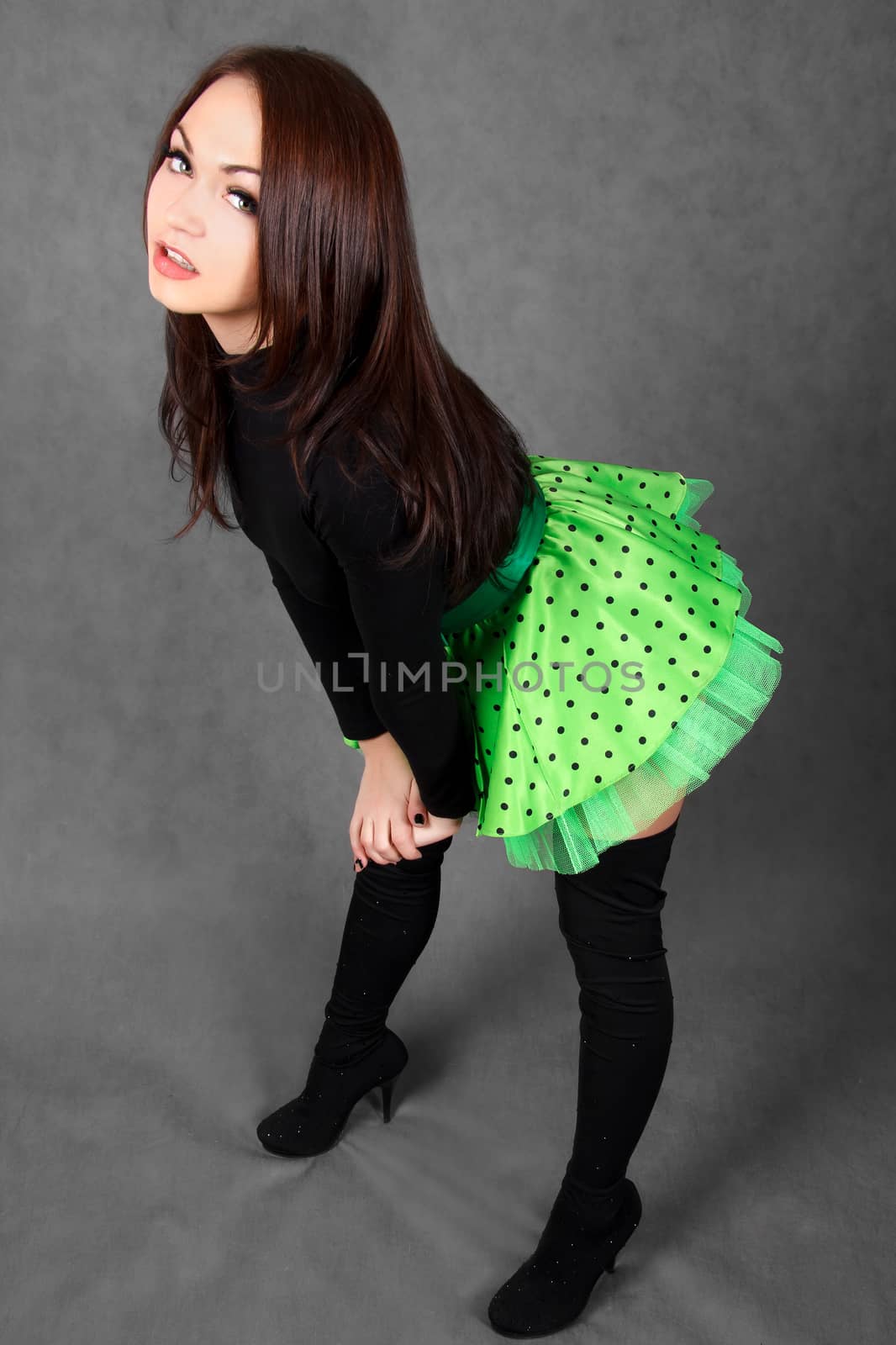 Portrait of a young attractive woman in a bright green skirt over grey background