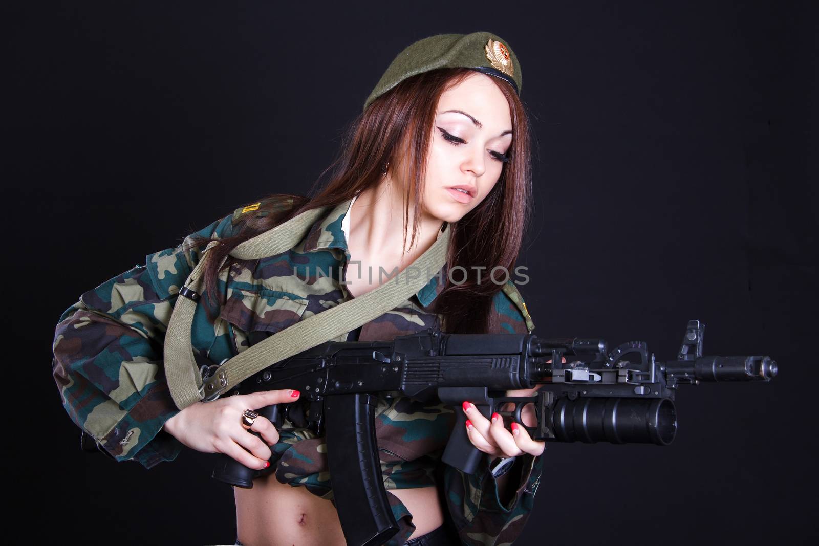 Young woman in the military uniform with the assault rifle over black background