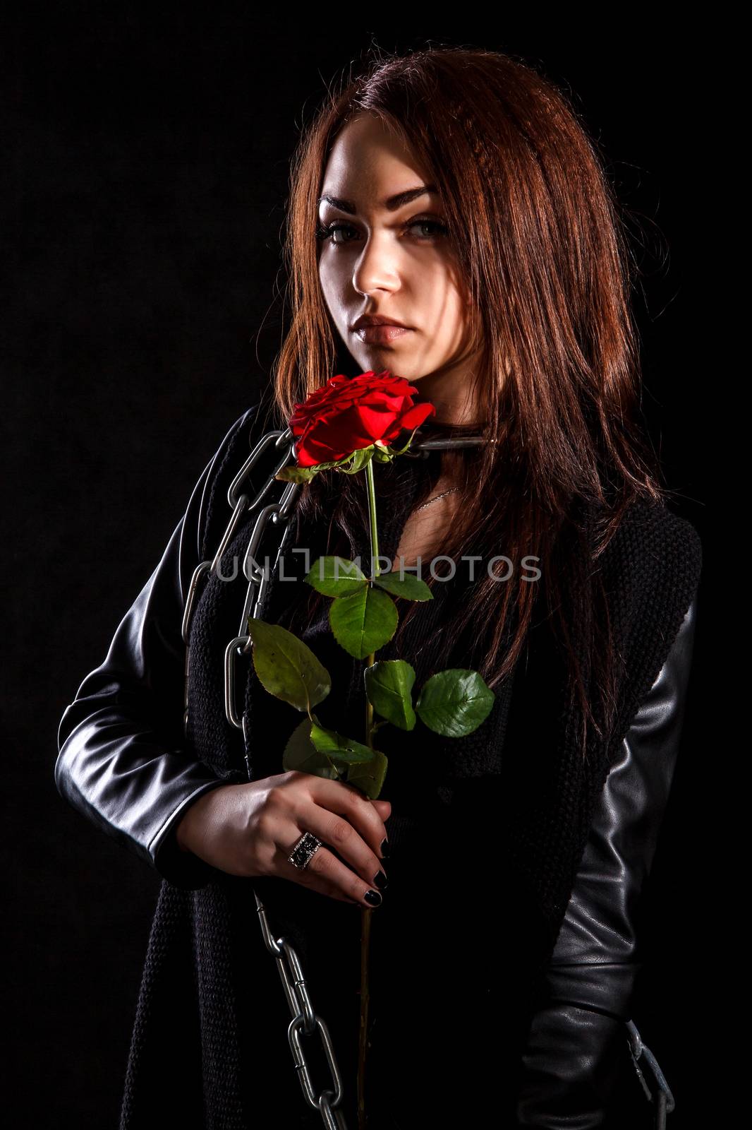 Beautiful young woman with a red rose in a black leather jacket over black background