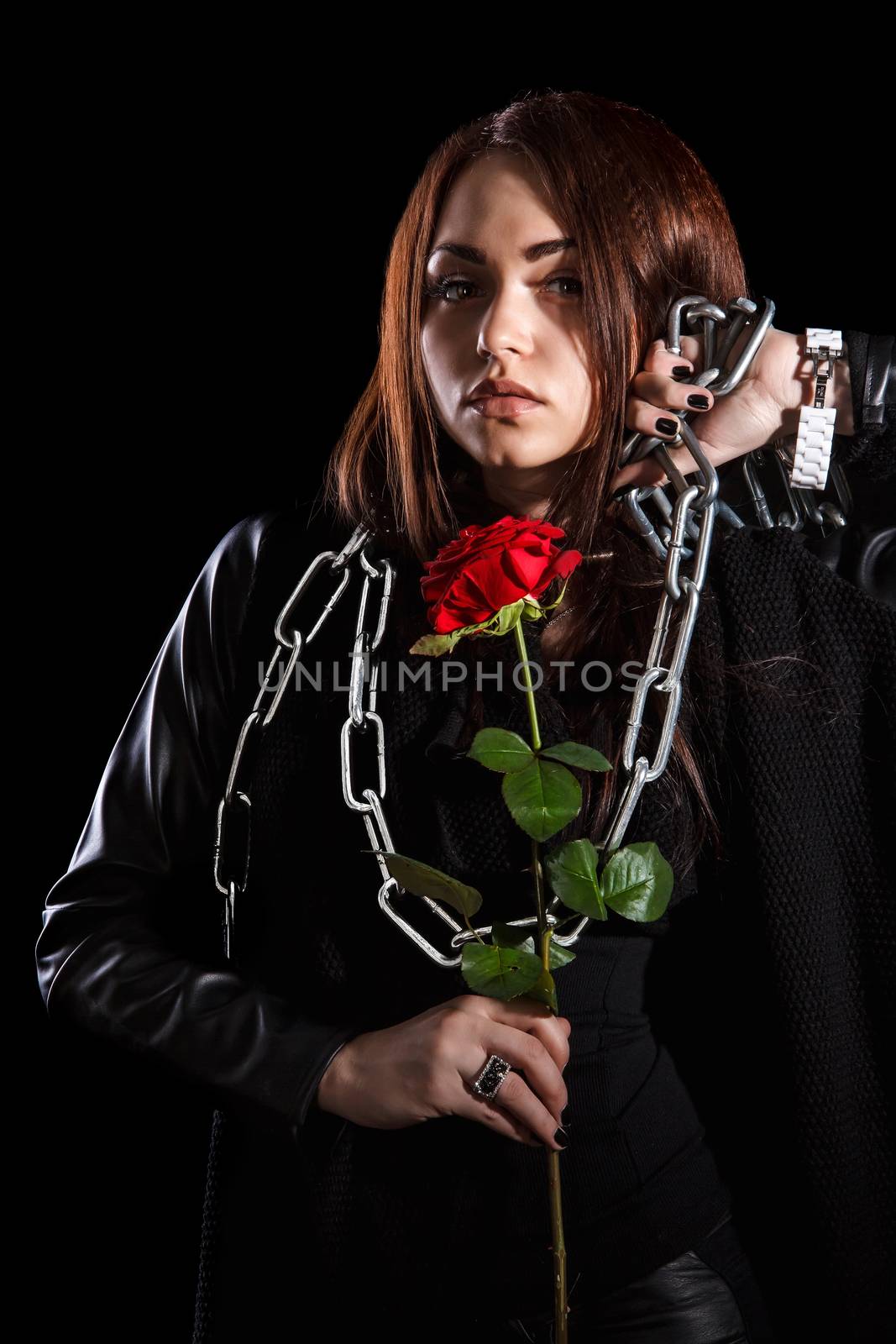 Beautiful young woman with chains and a red rose over black background