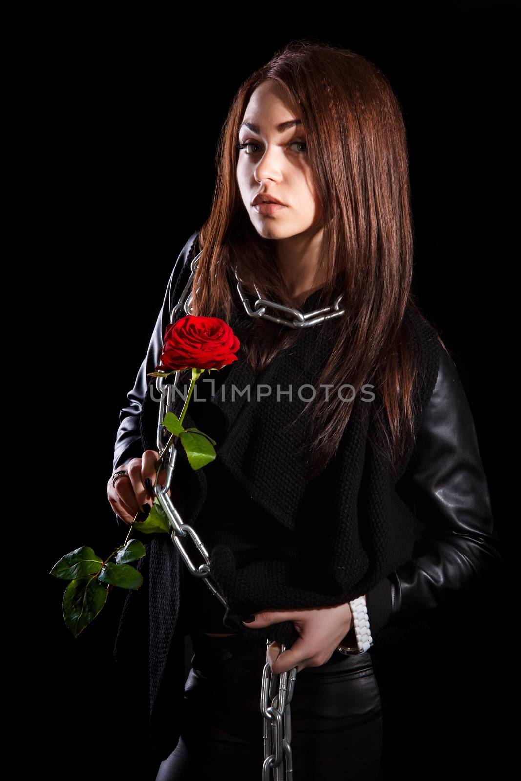 Beautiful young woman with chains and a red rose over black background