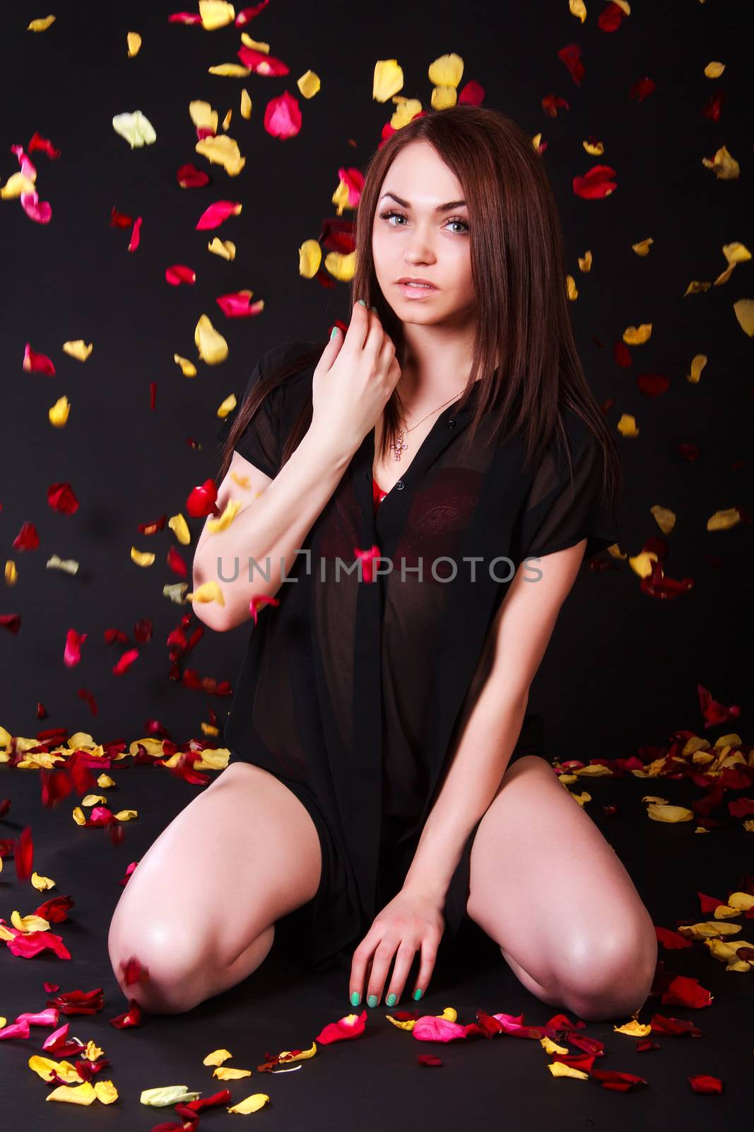 Beautiful young woman sitting under the falling petals over black background