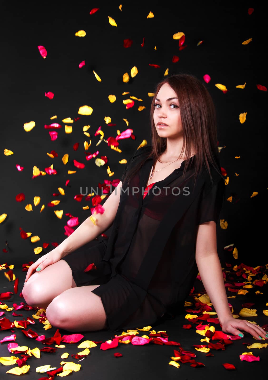 Beautiful young woman sitting under the falling petals over black background