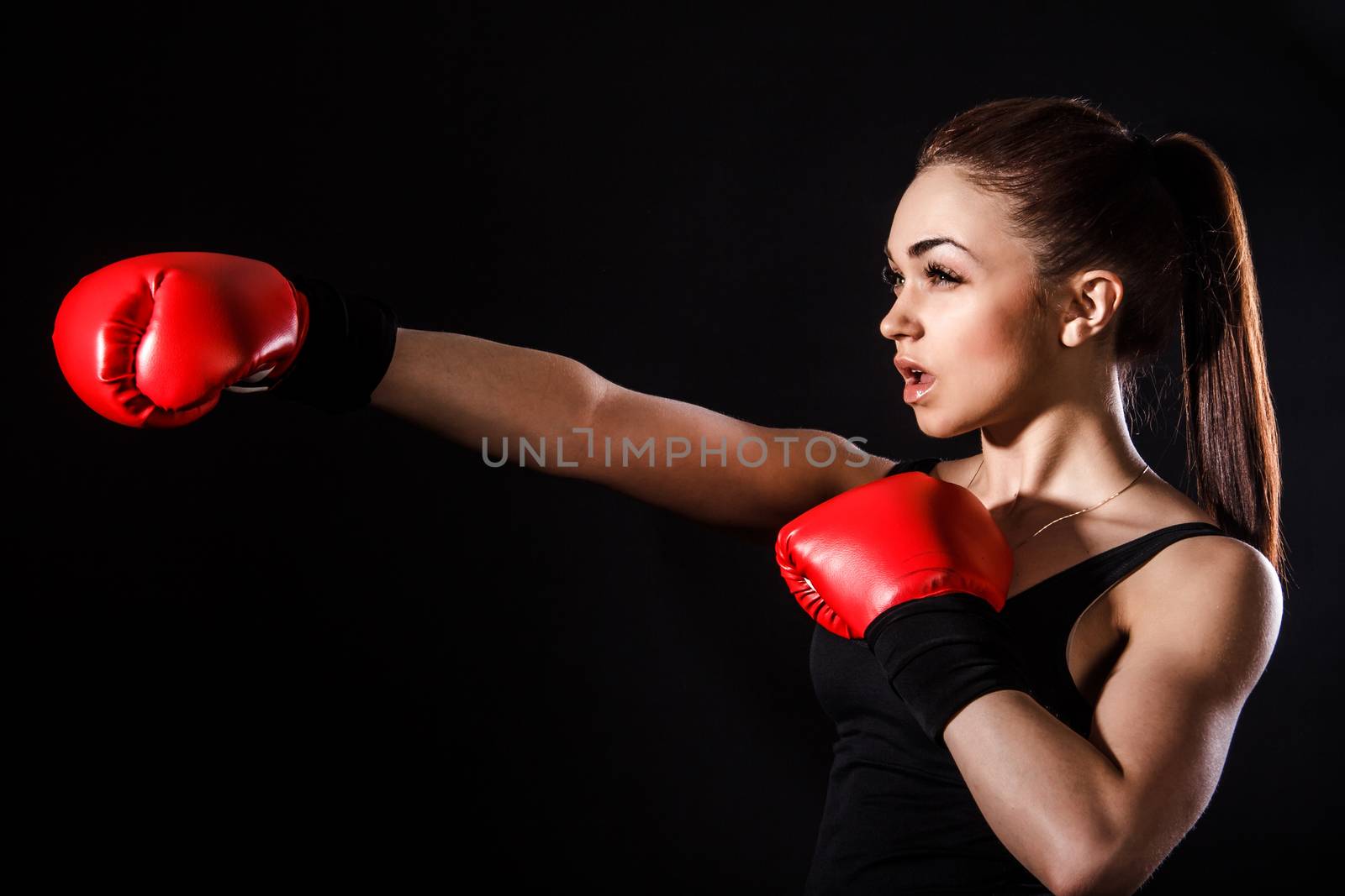 Beautiful young woman in a red boxing gloves over black background