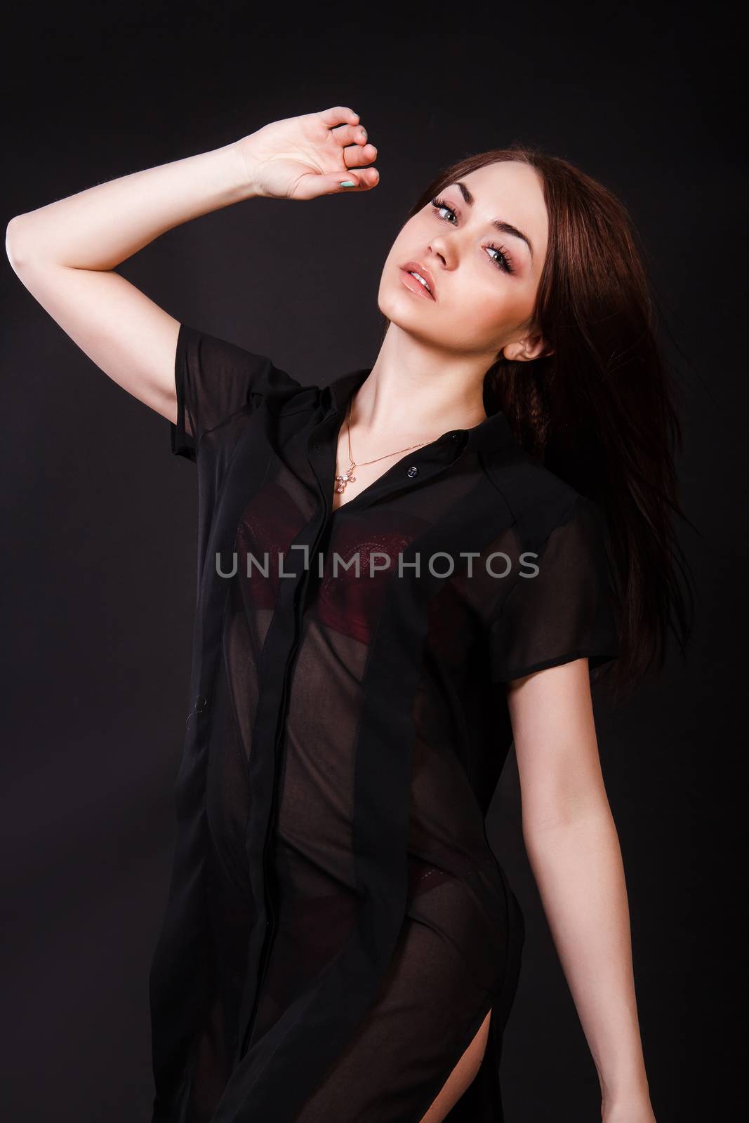 Amazing young woman in a red underwear and a black peignoir with a flying hair over black background