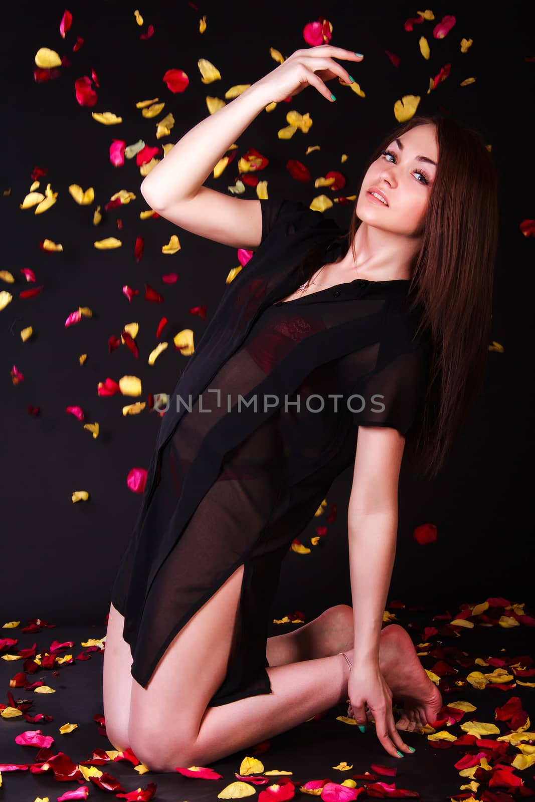 Beautiful young woman sitting under the falling petals over black background
