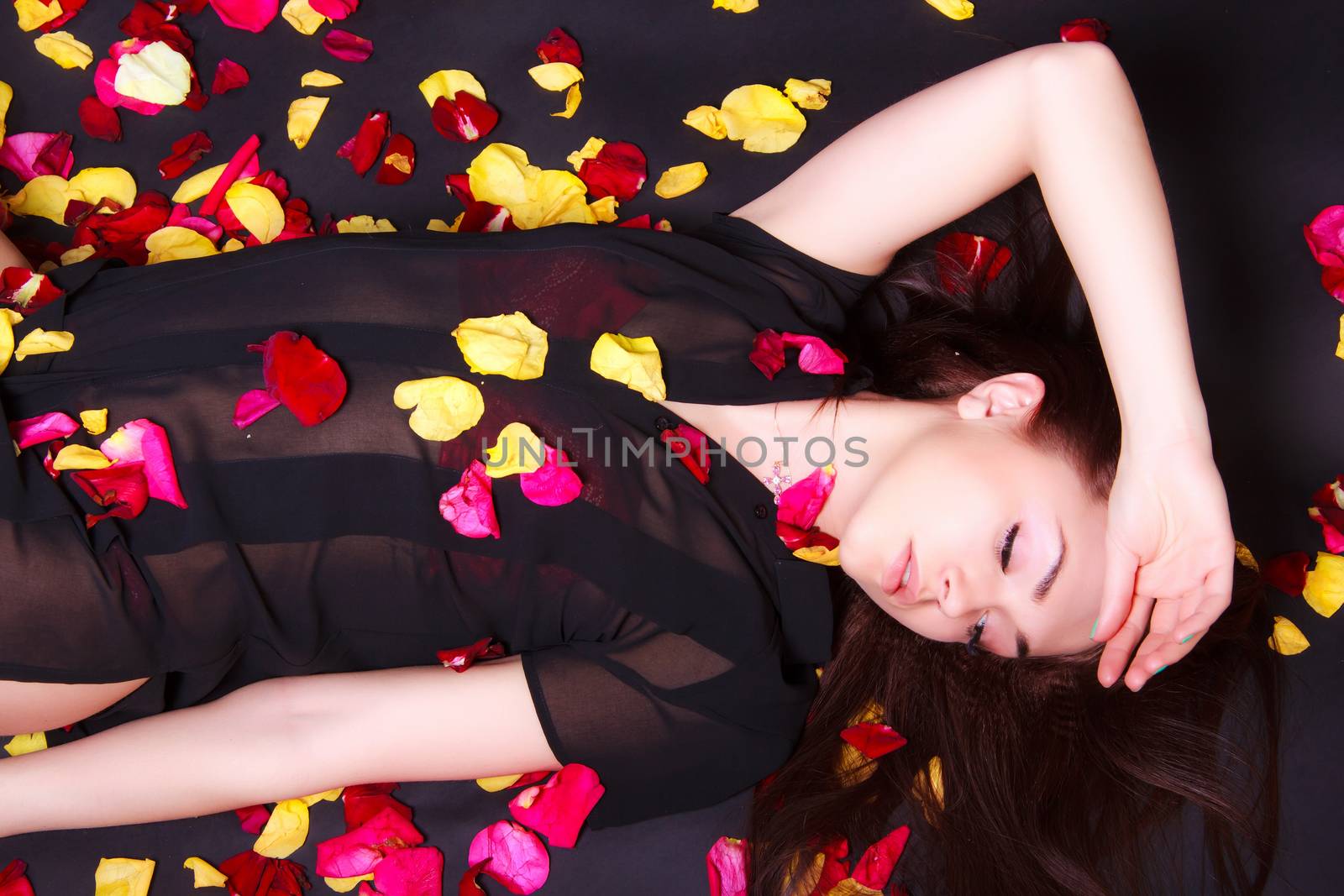 Beautiful young woman laying on sparse rose petals over black background