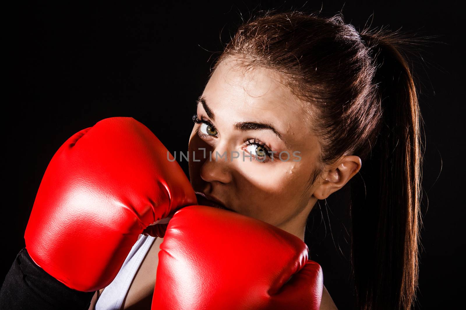 Beautiful young woman in a red boxing gloves over black background