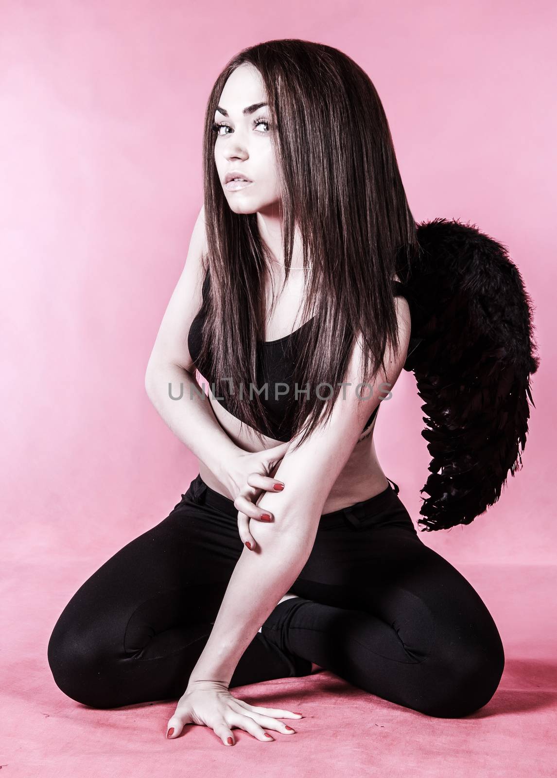 Beautiful young woman in a costume of the dark angel over pink background